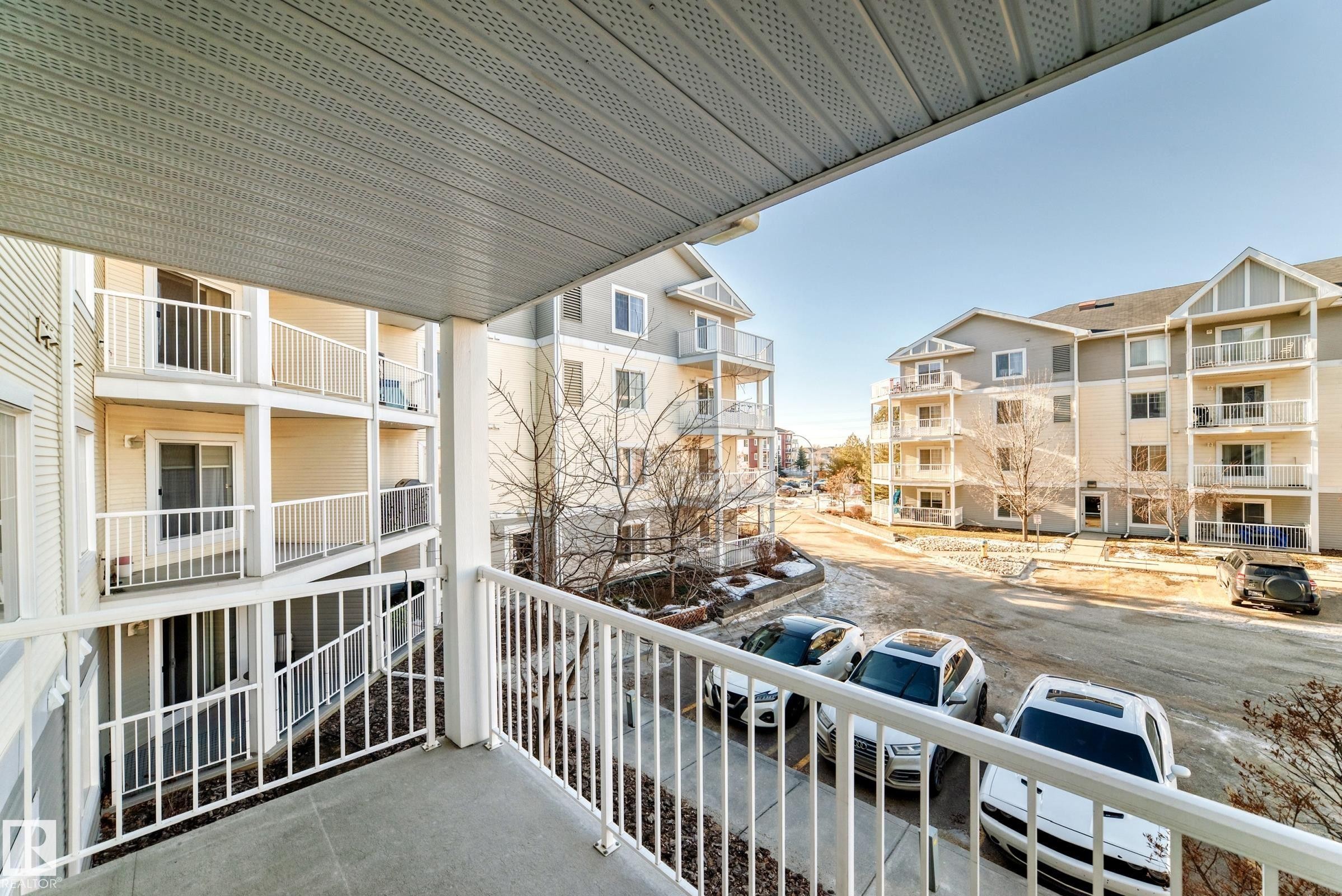 The property features a private balcony with white railings, offering views of the surrounding apartment buildings and parking areas - 208 2204 44 Ave, Edmonton, AB - Outdoor With Balcony With Exterior
