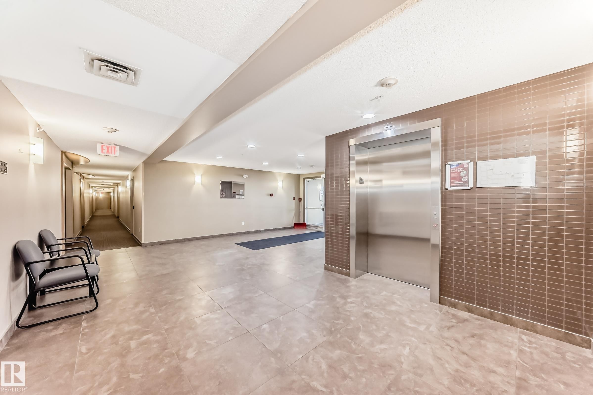 The property features a well-maintained common area with tiled flooring, a stainless steel elevator, and a long hallway - 208 2204 44 Ave, Edmonton, AB - Indoor Photo Showing Other Room