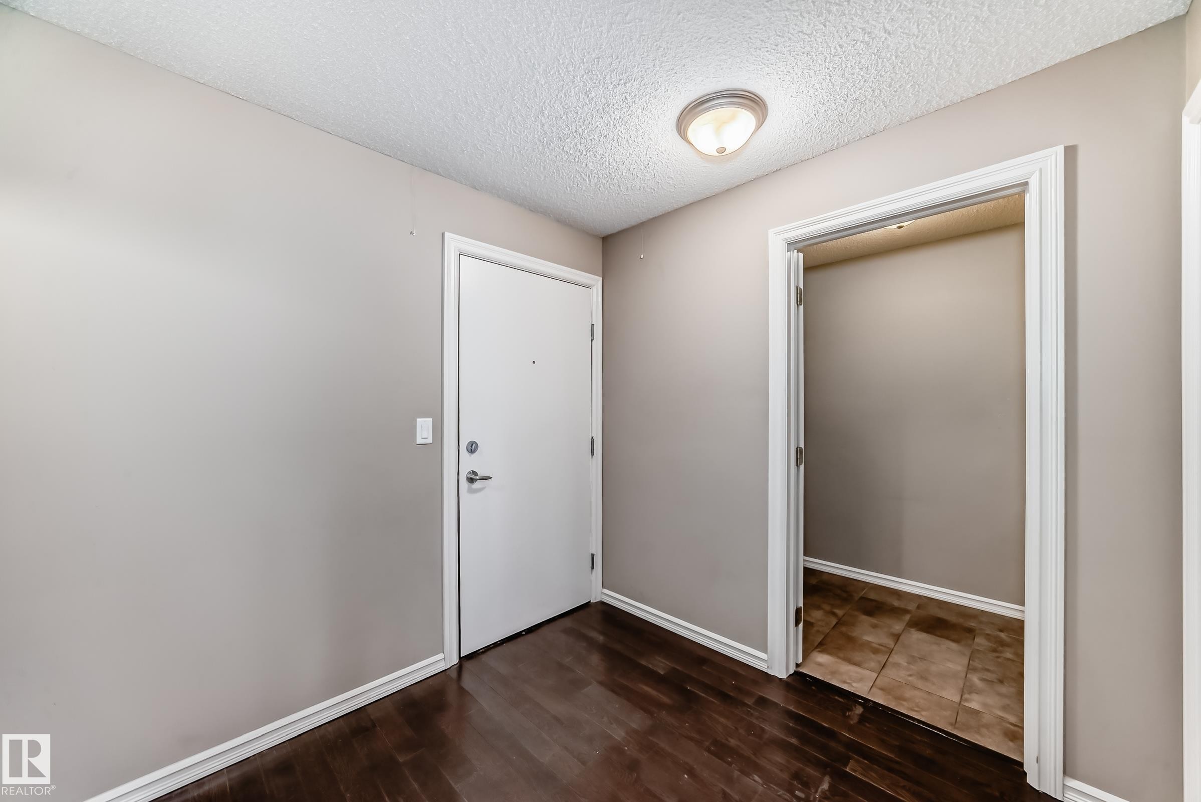 The entryway features dark wood flooring, a white door with silver hardware, and a ceiling-mounted light fixture - 208 2204 44 Ave, Edmonton, AB - Indoor Photo Showing Other Room