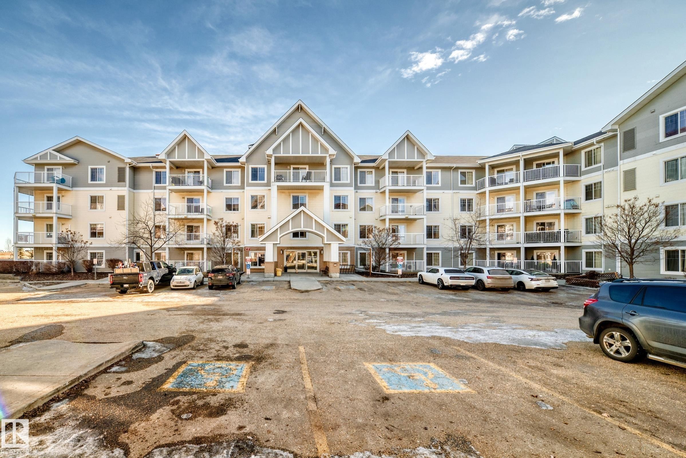 The property features a multi-story exterior with a combination of light and dark siding, numerous balconies with glass railings, and a prominent central entrance - 208 2204 44 Ave, Edmonton, AB - Outdoor With Balcony With Facade