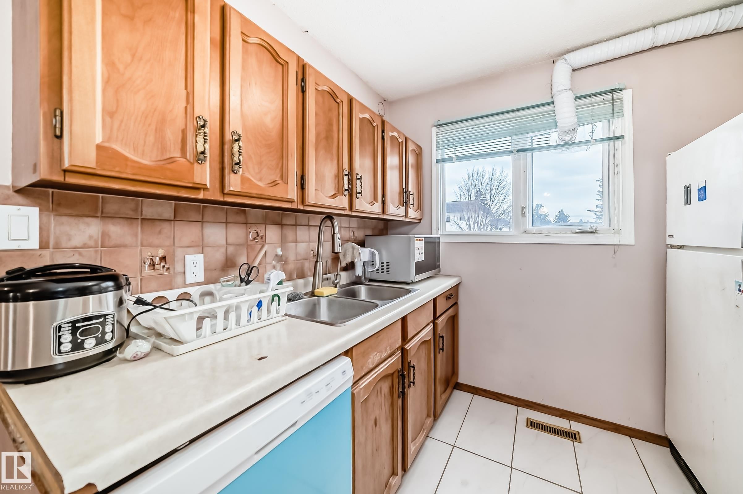 The kitchen features wood cabinetry, a tiled backsplash, a double basin sink, and a window providing natural light - 11393 22 Avenue, Edmonton, AB - Indoor Photo Showing Kitchen With Double Sink