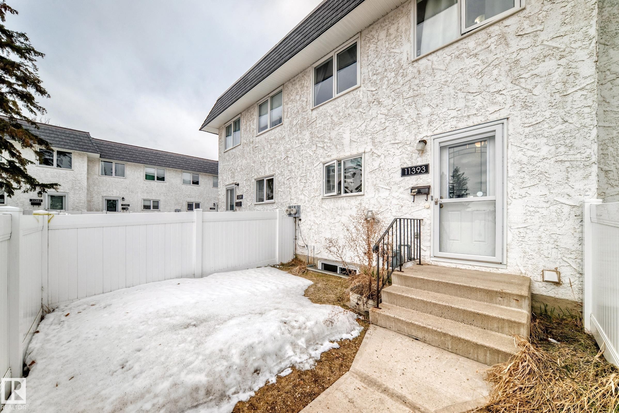 The property features a private fenced yard, a concrete walkway leading to the entrance, and concrete steps with a black metal handrail - 11393 22 Avenue, Edmonton, AB - Outdoor