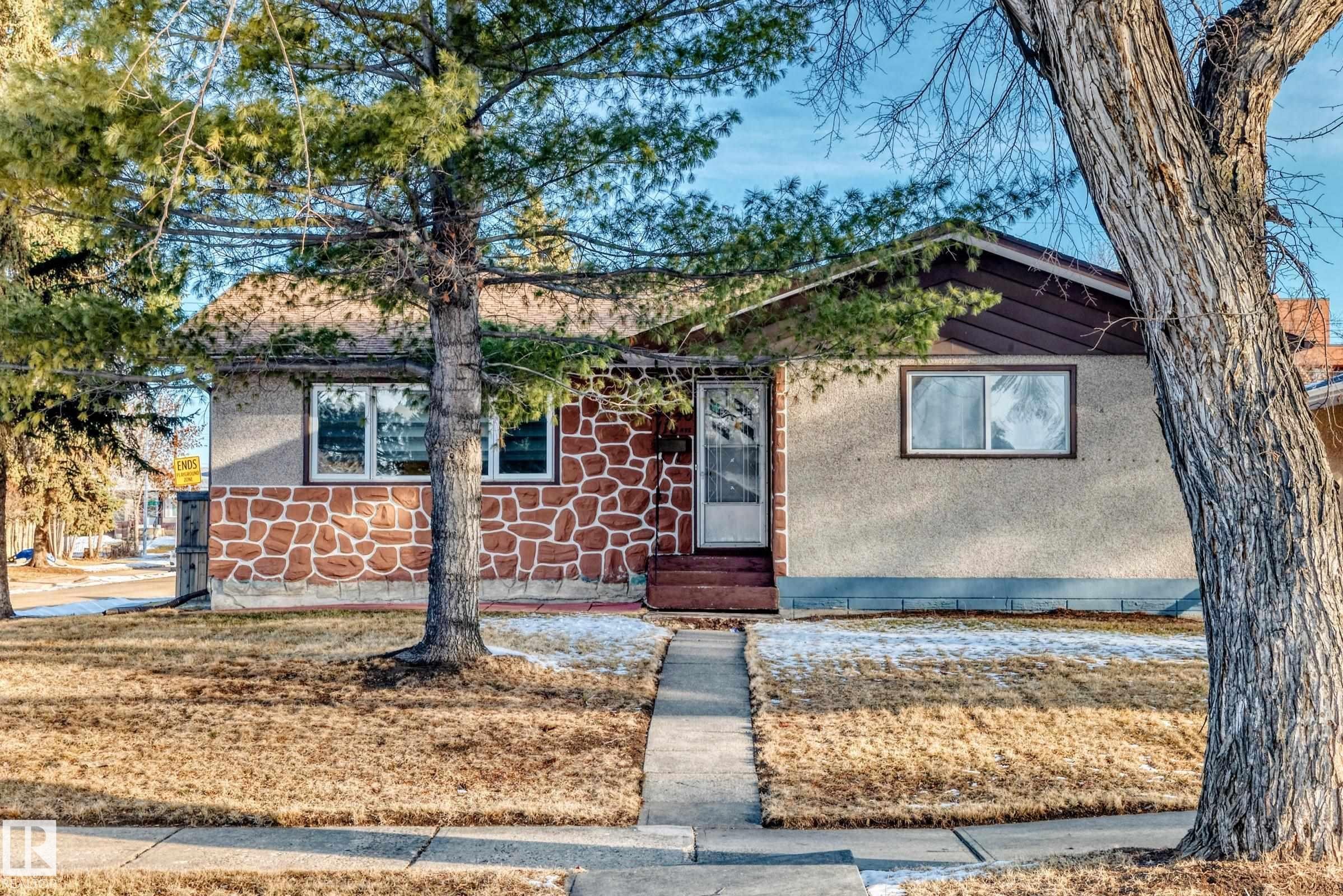 The property features a concrete walkway leading to the entrance, a stone veneer facade, and a small front yard with trees - 4446 116 Avenue, Edmonton, AB - Outdoor