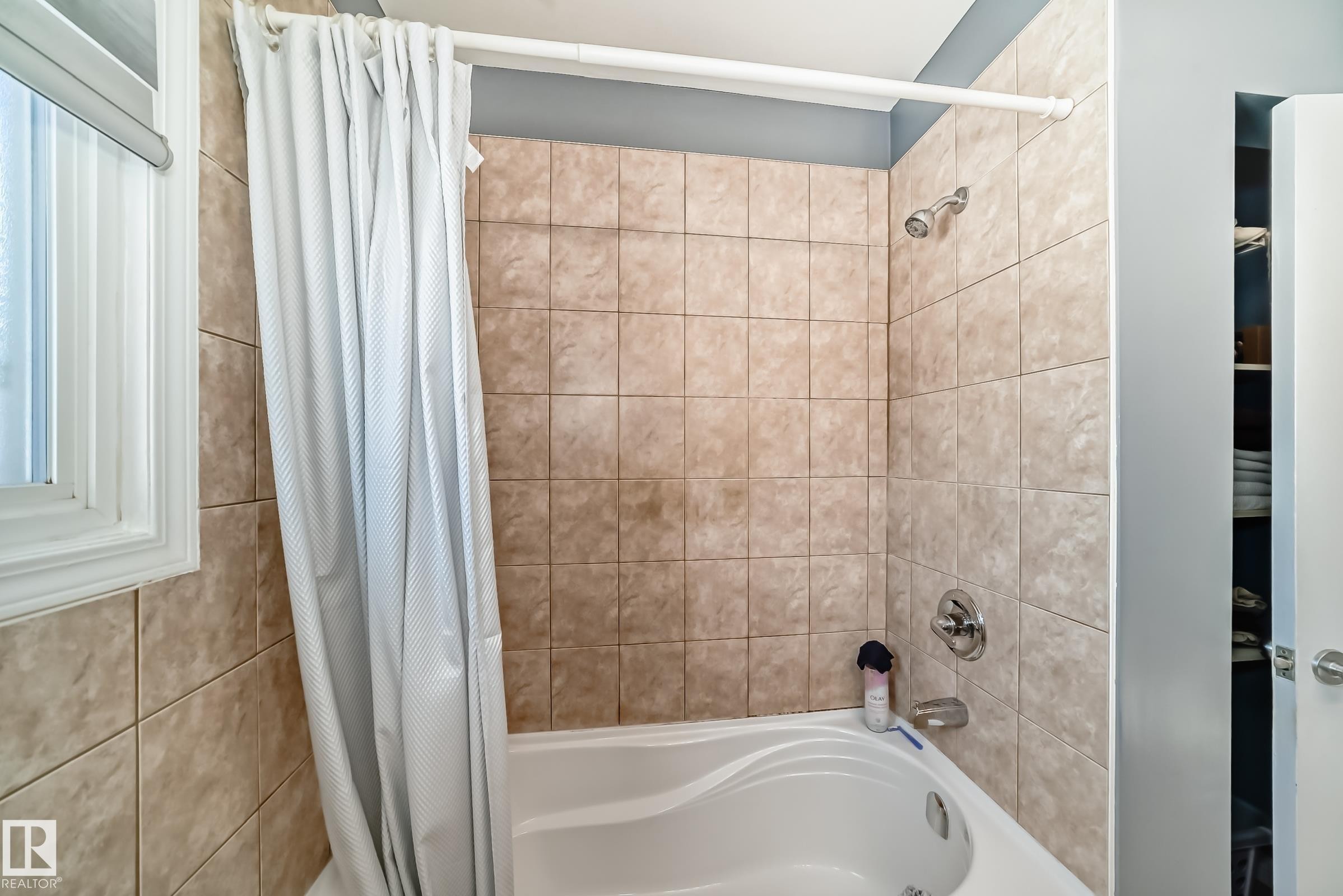 Bathroom featuring a built-in bathtub with a tile surround and a window providing natural light - 4446 116 Avenue, Edmonton, AB - Indoor Photo Showing Bathroom