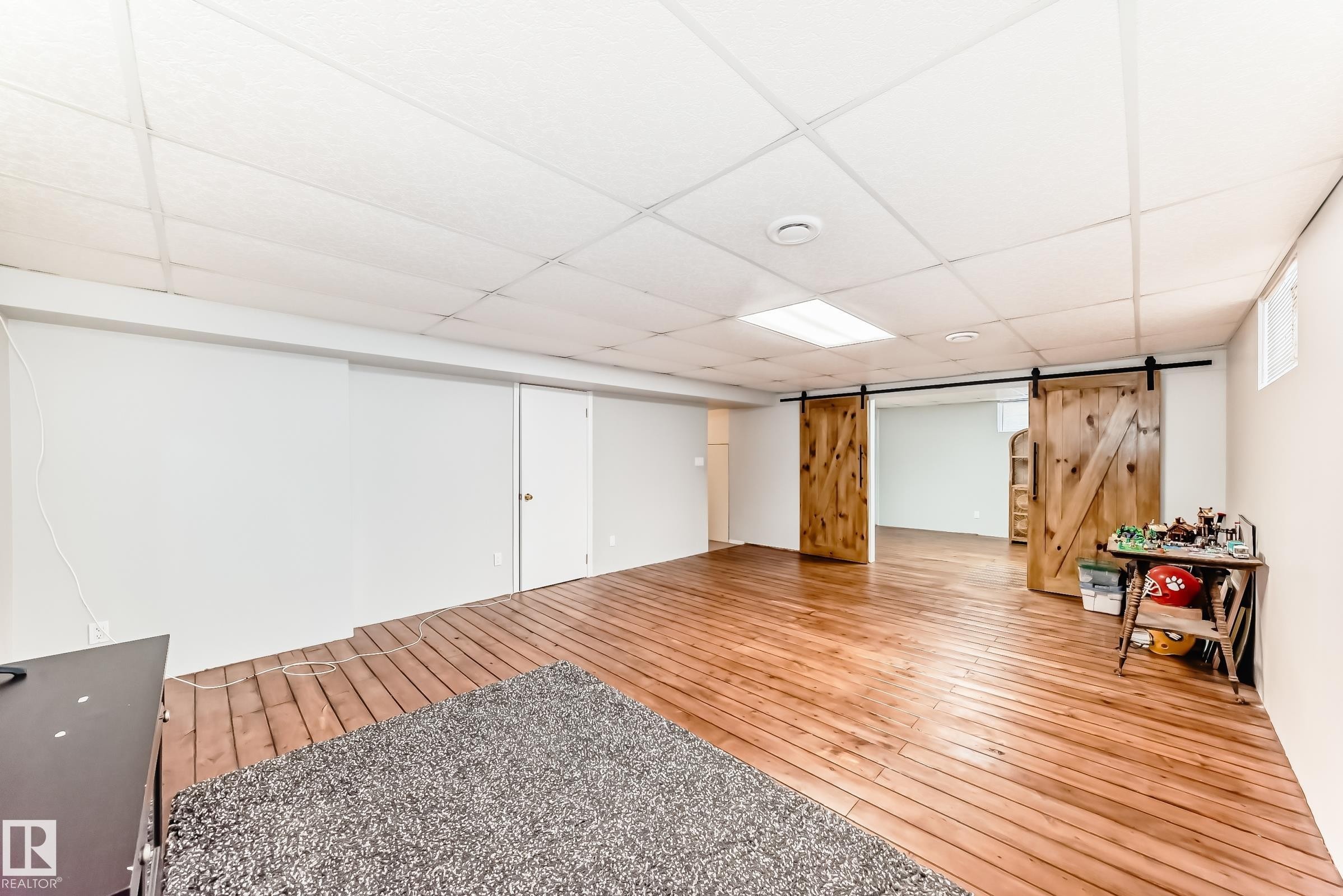 This expansive room features wide plank wood flooring and modern barn-style sliding doors, enhancing its unique appeal - 4446 116 Avenue, Edmonton, AB - Indoor Photo Showing Other Room