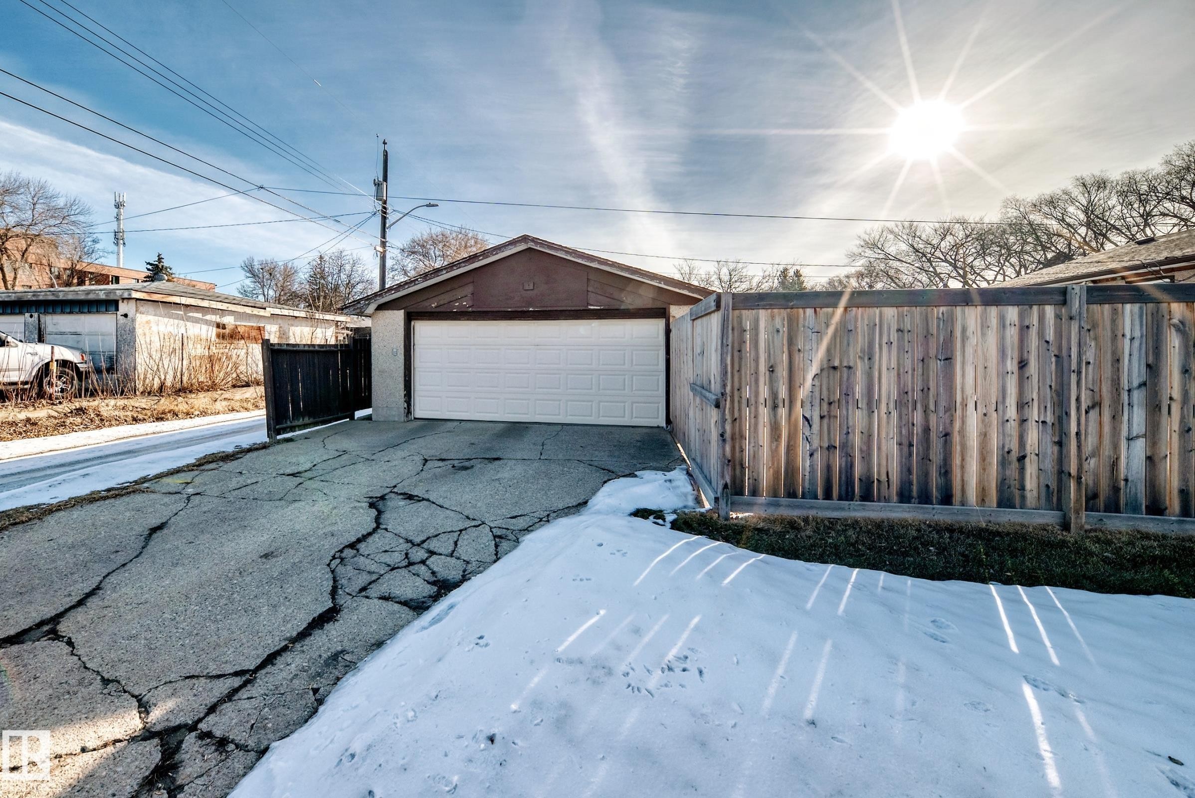 The property features a detached garage with a white garage door, a wooden privacy fence, and a paved driveway - 4446 116 Avenue, Edmonton, AB - Outdoor