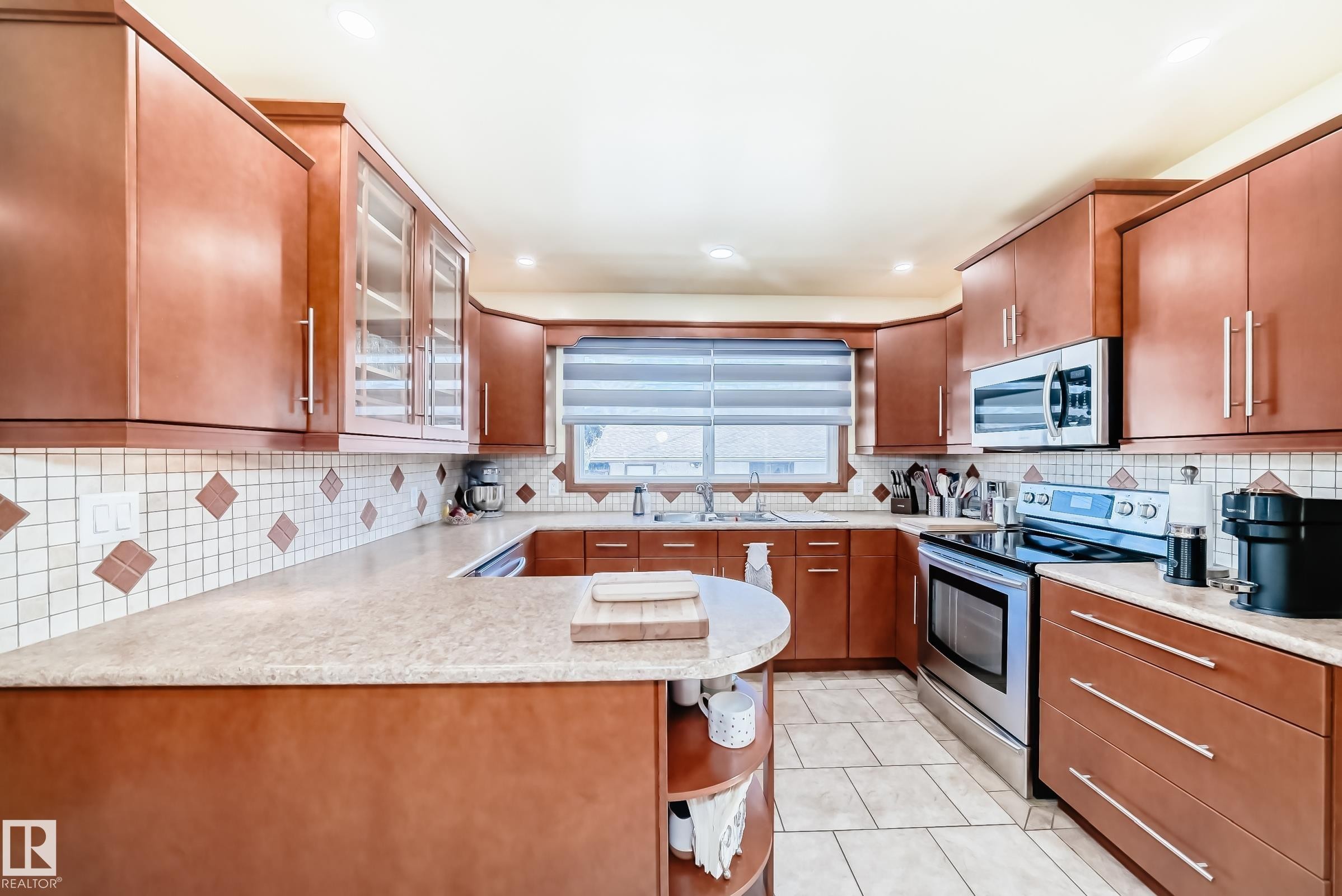 The property features a kitchen with wood cabinetry, a tiled backsplash with decorative accents, and light-colored countertops - 4446 116 Avenue, Edmonton, AB - Indoor Photo Showing Kitchen With Double Sink