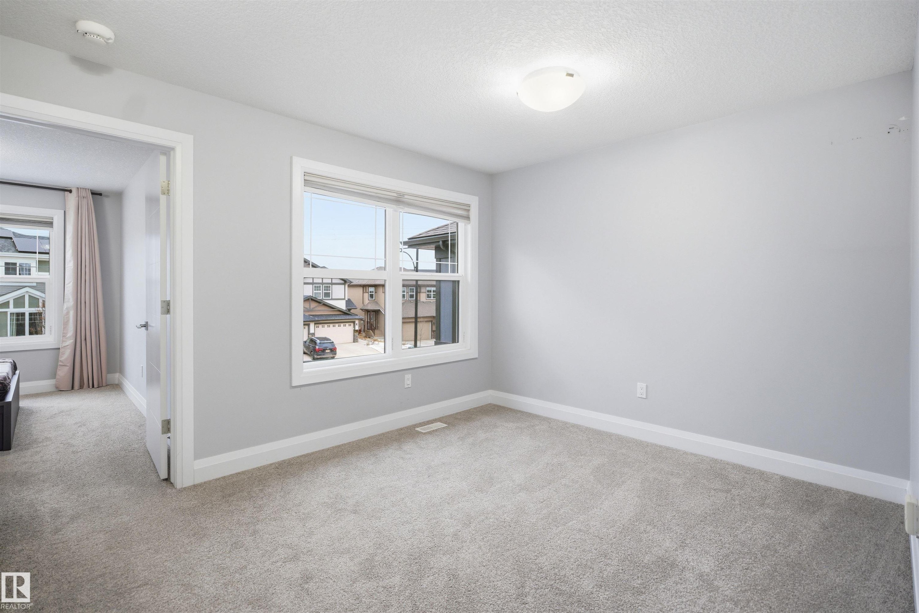 The room features light gray carpeting, neutral wall paint, and a window with a view of the surrounding properties - 8424 Cushing Court, Edmonton, AB - Indoor Photo Showing Other Room