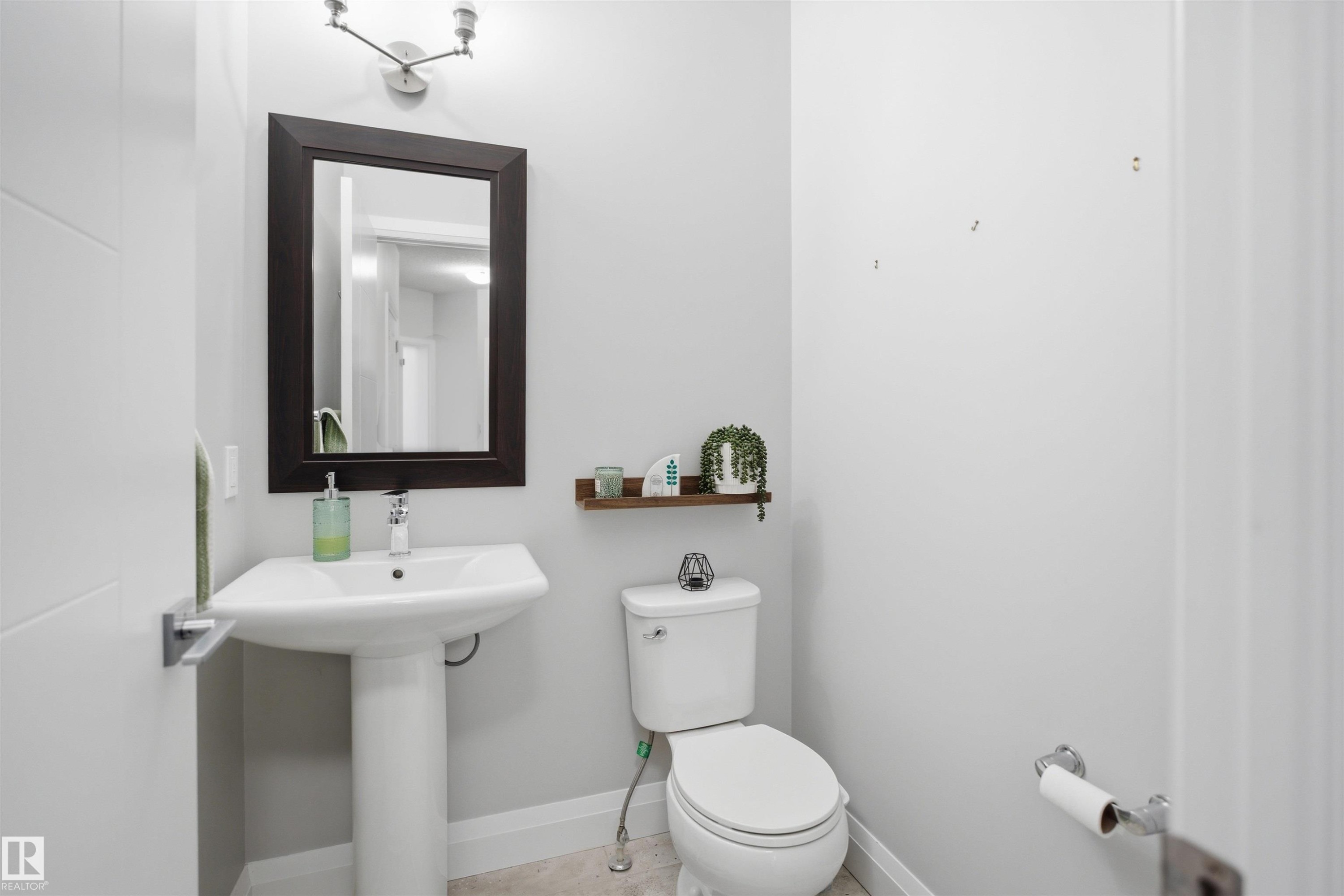 Bathroom with a pedestal sink, a toilet, a mirror with a dark frame, and a wall-mounted light fixture - 8424 Cushing Court, Edmonton, AB - Indoor Photo Showing Bathroom