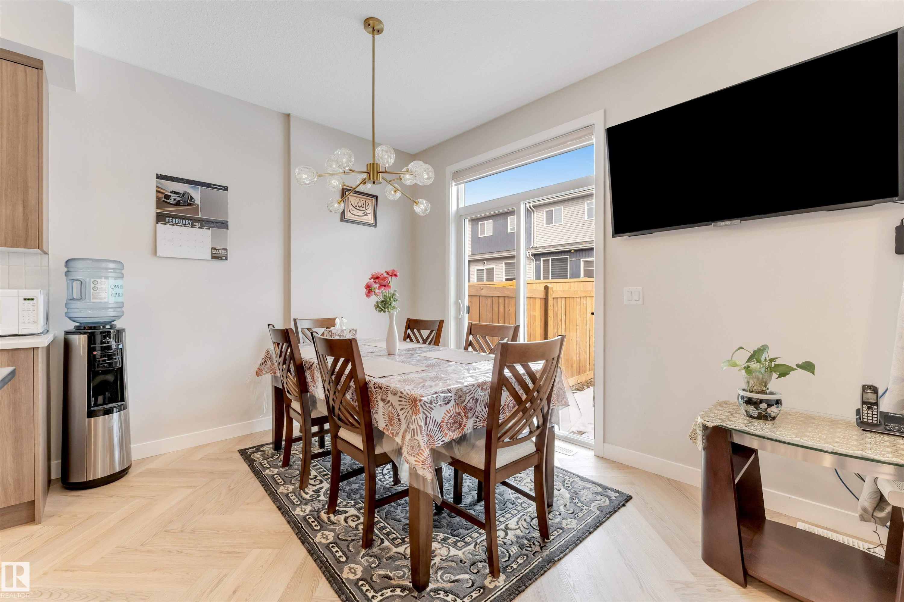 The dining area features light-toned herringbone flooring, a modern chandelier, and sliding glass doors that open to a fenced outdoor area - 6404 27 Avenue, Edmonton, AB - Indoor Photo Showing Dining Room