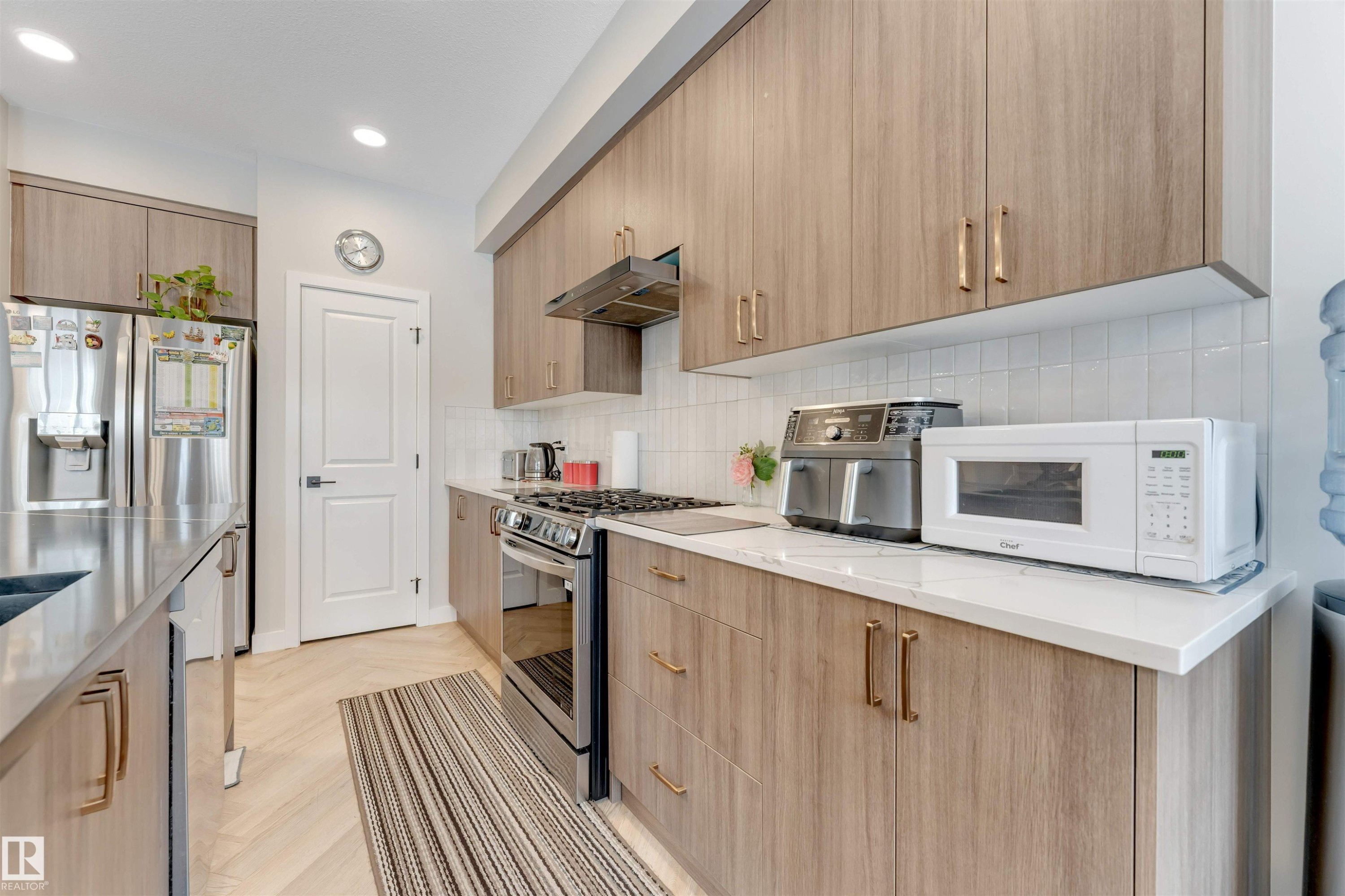 The kitchen features light wood cabinetry with gold-toned hardware, stainless steel appliances, a white tile backsplash, and a light-colored countertop - 6404 27 Avenue, Edmonton, AB - Indoor Photo Showing Kitchen With Upgraded Kitchen