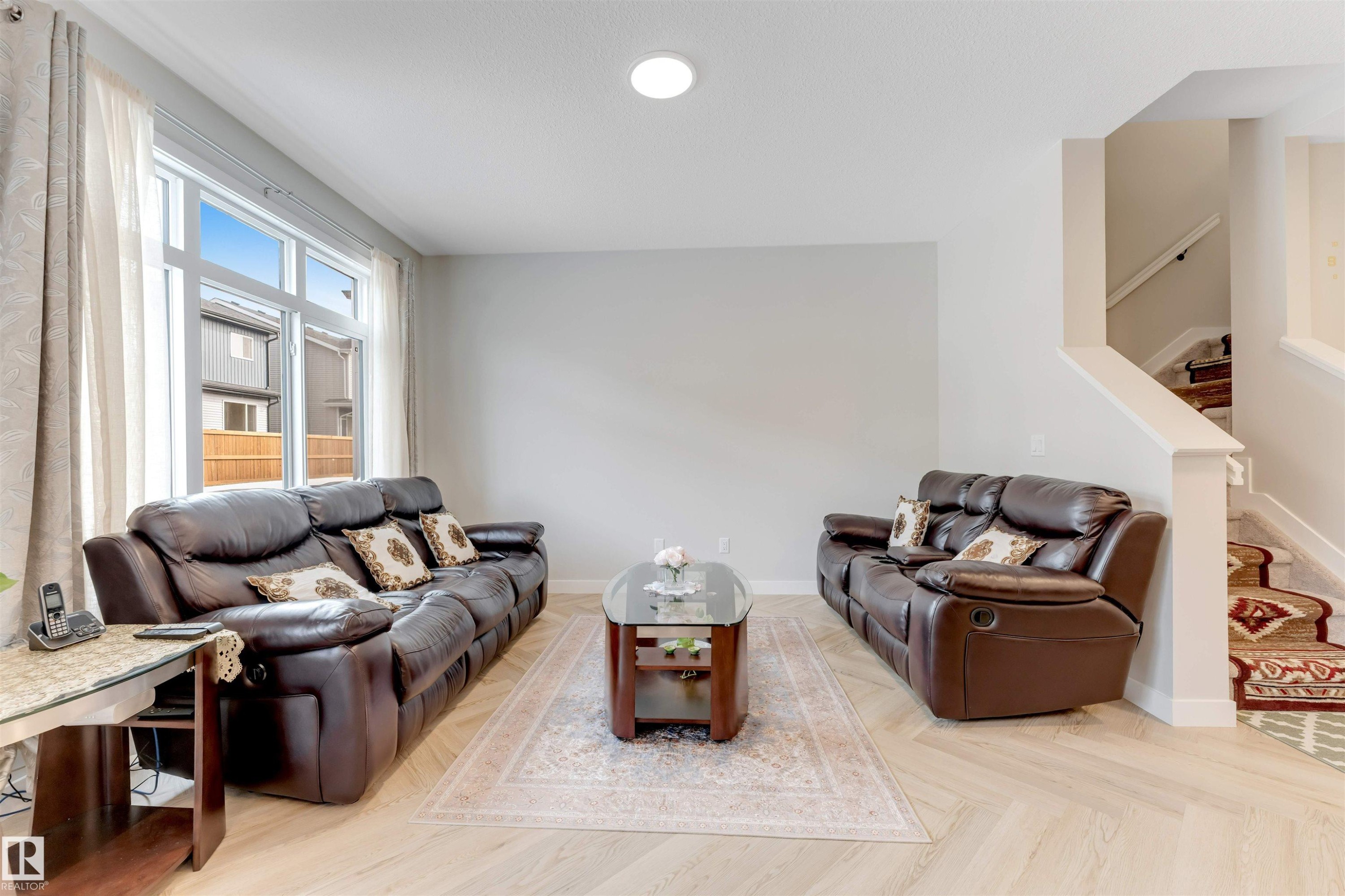 Living area featuring light-colored flooring, a large window, and a staircase with patterned carpet - 6404 27 Avenue, Edmonton, AB - Indoor Photo Showing Other Room