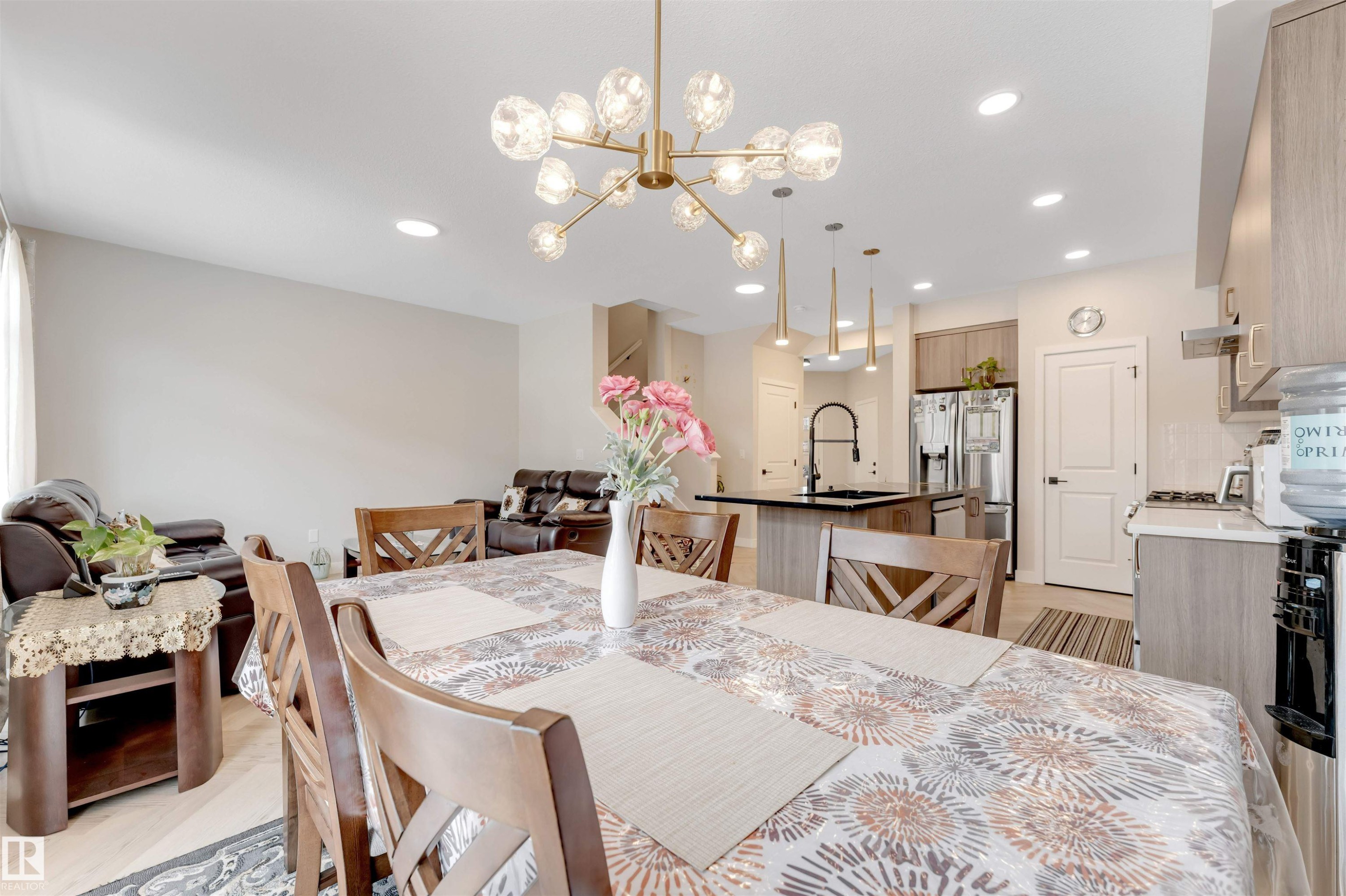 The open concept living area includes a dining space with a contemporary chandelier and a kitchen featuring an island with a sink and pendant lighting - 6404 27 Avenue, Edmonton, AB - Indoor Photo Showing Dining Room