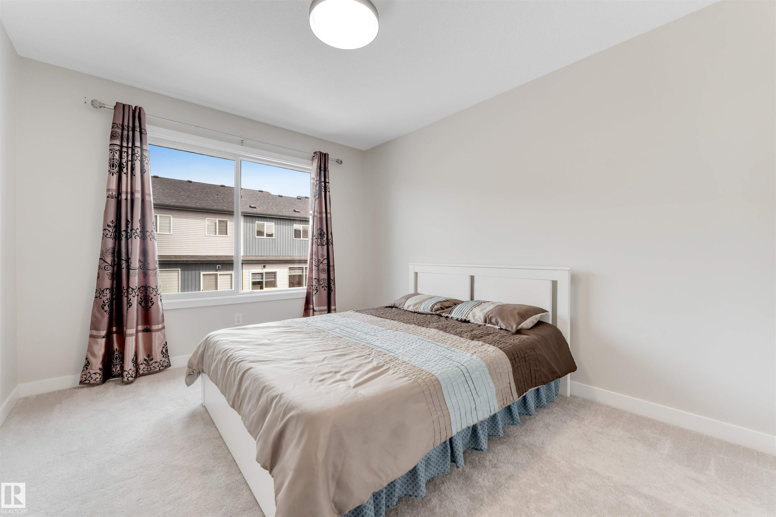 This bedroom features light-colored walls, a large window with patterned curtains, and a light-colored carpet - 6404 27 Avenue, Edmonton, AB - Indoor Photo Showing Bedroom
