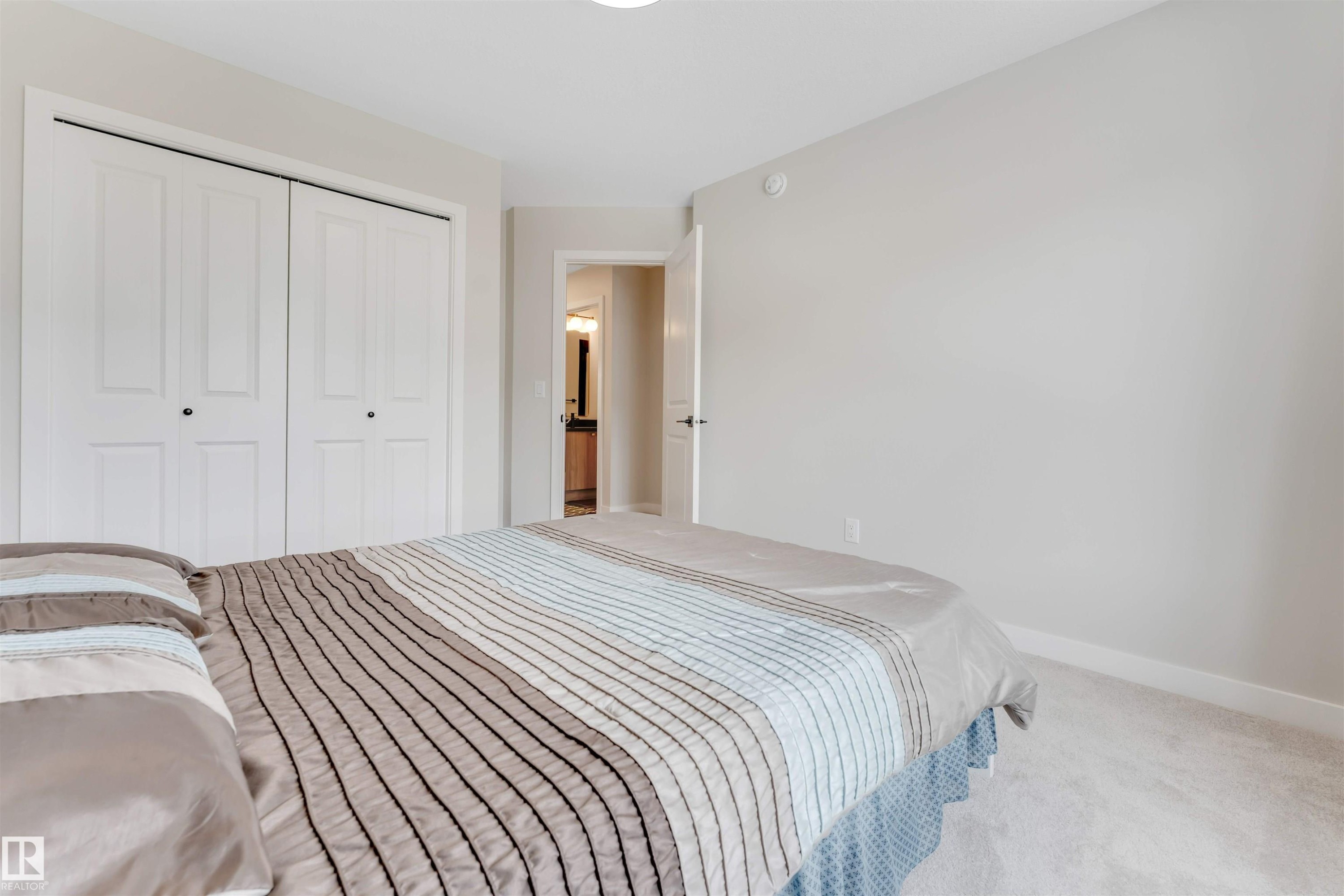 The room features light-colored walls and carpeting, a closet with white bi-fold doors, and a doorway leading to a room with a vanity - 6404 27 Avenue, Edmonton, AB - Indoor Photo Showing Bedroom