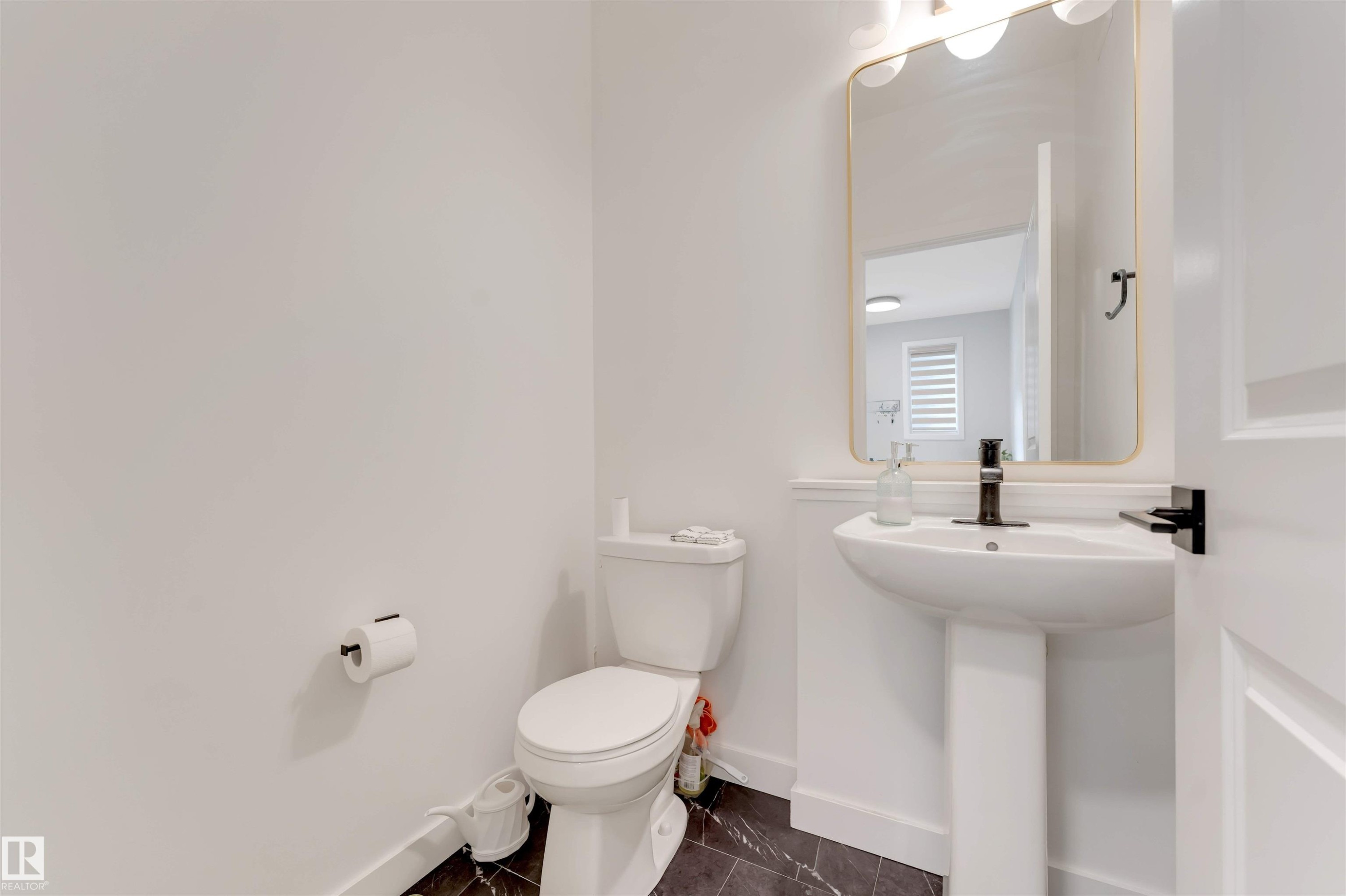 The property features a powder room with a pedestal sink, a rectangular mirror with a gold-toned frame, and a modern black faucet - 6404 27 Avenue, Edmonton, AB - Indoor Photo Showing Bathroom