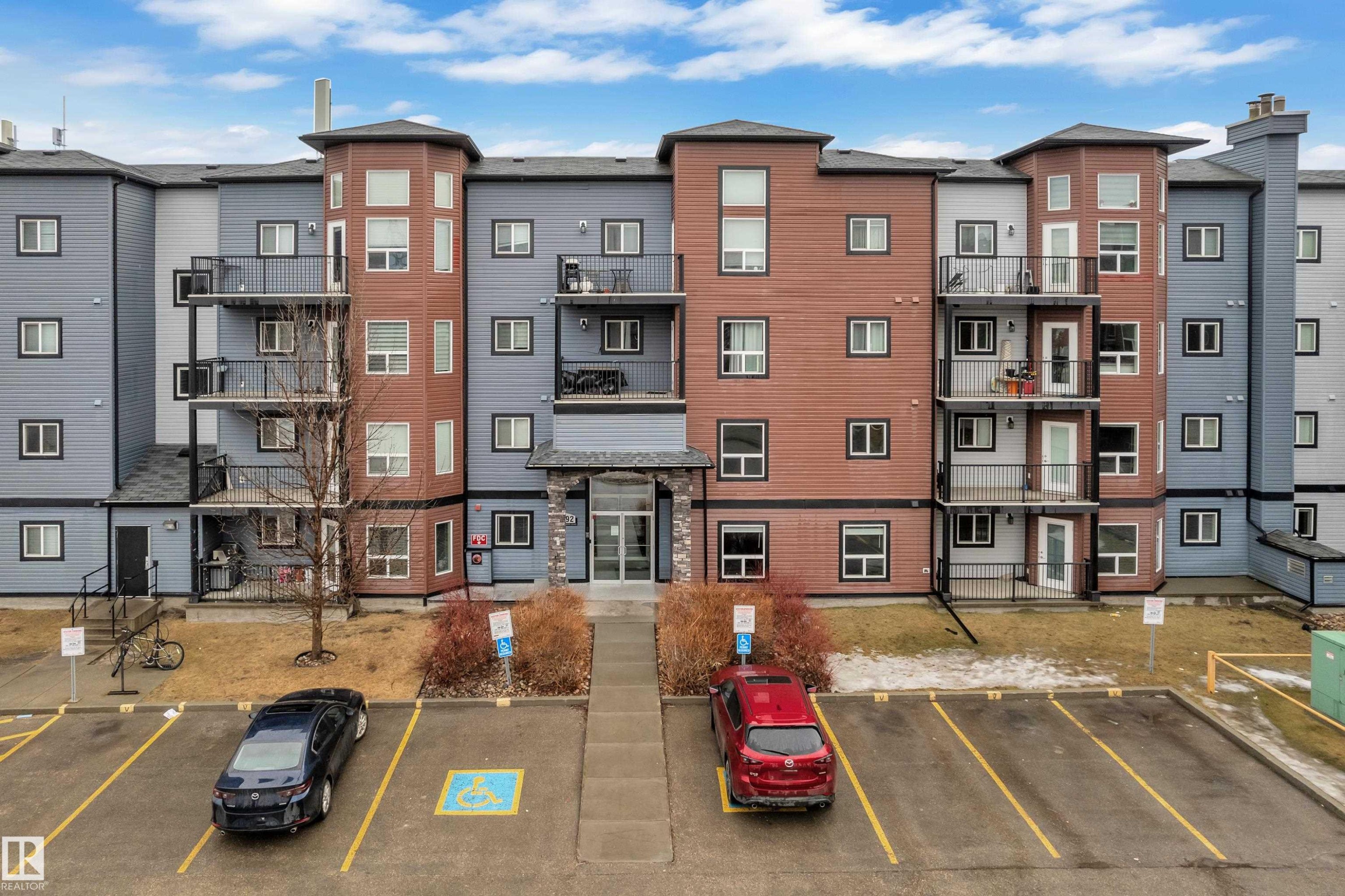 The property features a multi-story building with a facade combining grey siding and reddish-brown paneling, accented by black trim around the windows and balconies - 320 392 Silver Berry Road, Edmonton, AB - Outdoor With Facade