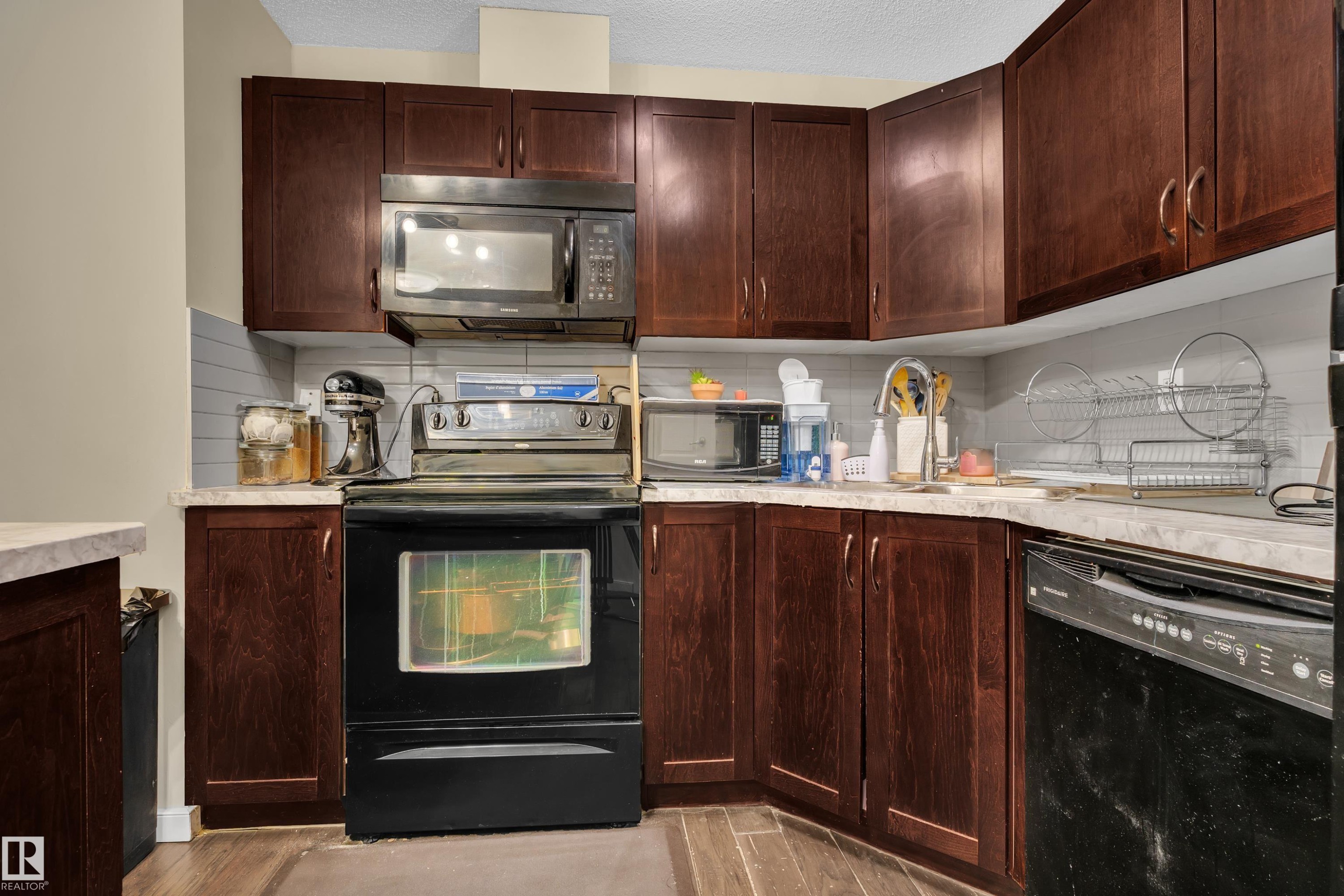 The kitchen features dark wood cabinetry, a stainless steel microwave, a black range with an oven, and a black dishwasher - 320 392 Silver Berry Road, Edmonton, AB - Indoor Photo Showing Kitchen