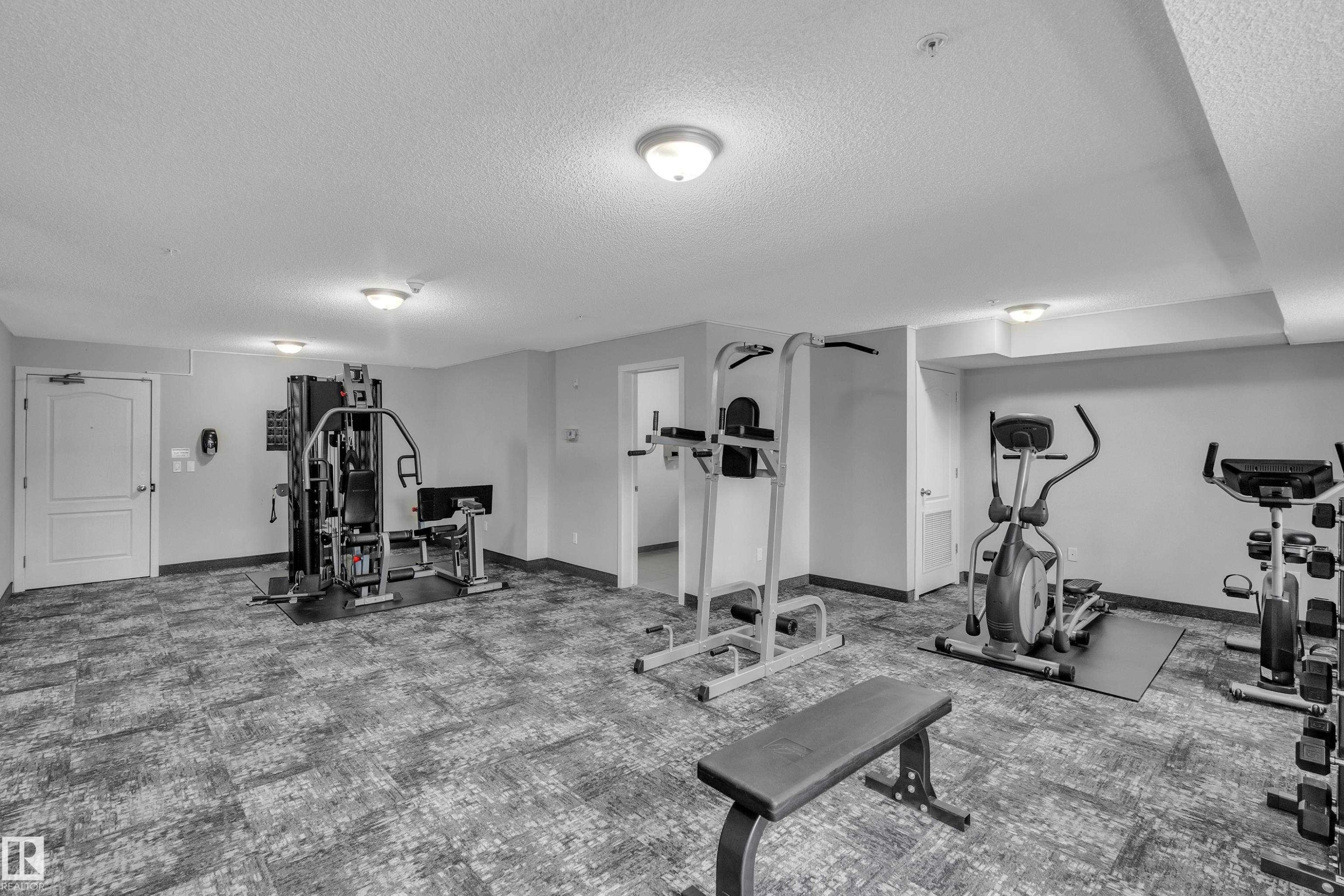 The property features a dedicated fitness area with various exercise equipment, including a multi-station gym, an elliptical machine, and a stationary bicycle - 320 392 Silver Berry Road, Edmonton, AB - Indoor Photo Showing Gym Room