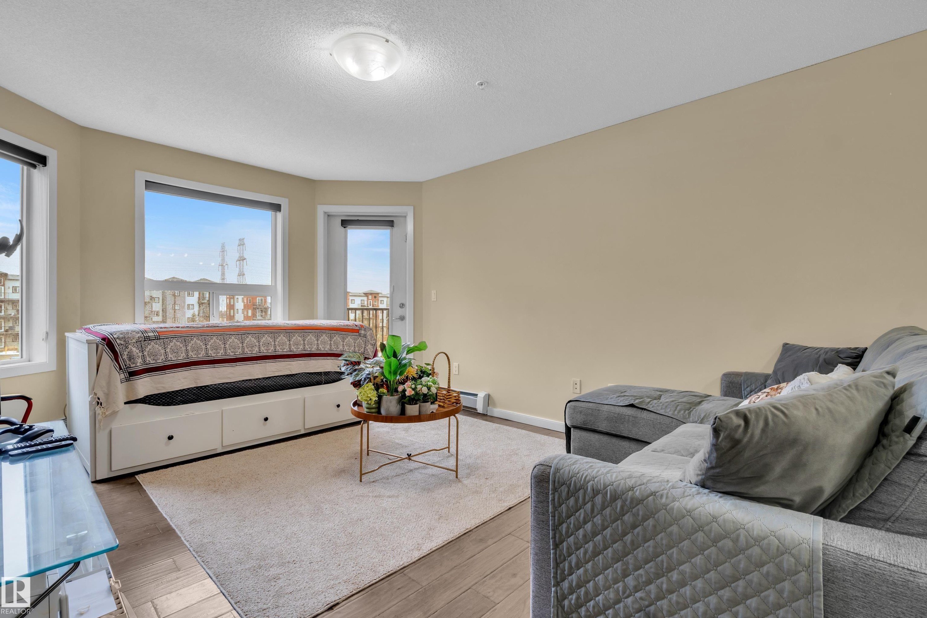 The living area features light-colored walls, hardwood flooring, and a large window providing views of the distant buildings and landscape - 320 392 Silver Berry Road, Edmonton, AB - Indoor
