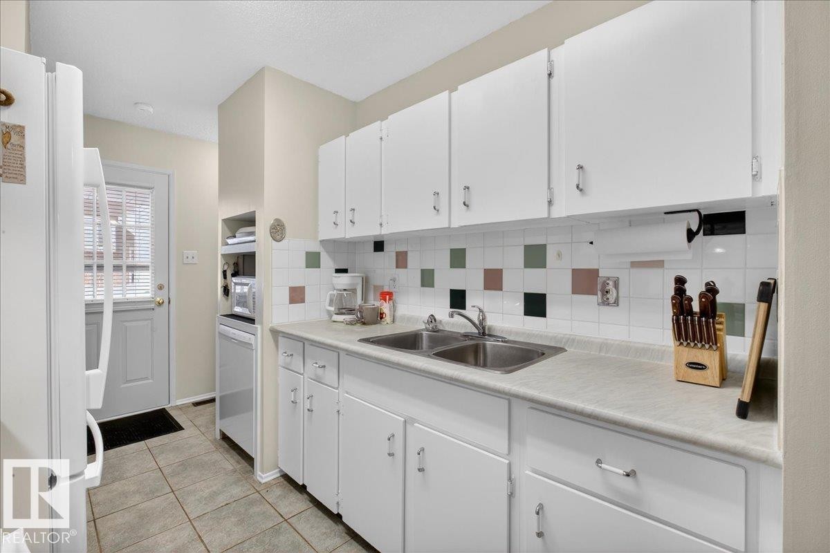 The kitchen features white cabinetry, a double basin sink, and a tiled backsplash with decorative square accents - 2 Mcleod Place, Edmonton, AB - Indoor Photo Showing Kitchen With Double Sink