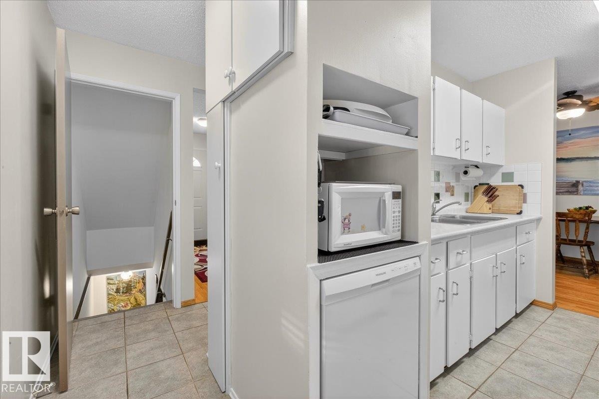 The kitchen features white cabinetry, a sink, and a tiled backsplash, with a dishwasher integrated below the counter - 2 Mcleod Place, Edmonton, AB - Indoor Photo Showing Kitchen