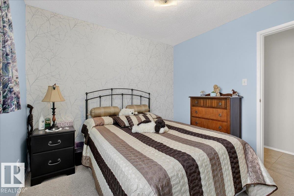 The room features a textured accent wall, light blue painted walls, and an overhead light fixture - 2 Mcleod Place, Edmonton, AB - Indoor Photo Showing Bedroom