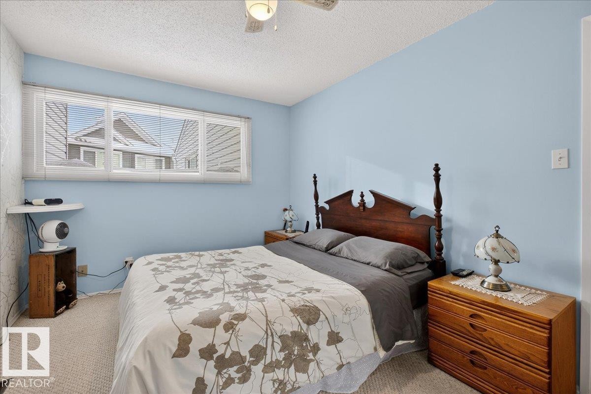 The room features light blue walls, a window with horizontal blinds, and a textured ceiling with a ceiling fan - 2 Mcleod Place, Edmonton, AB - Indoor Photo Showing Bedroom