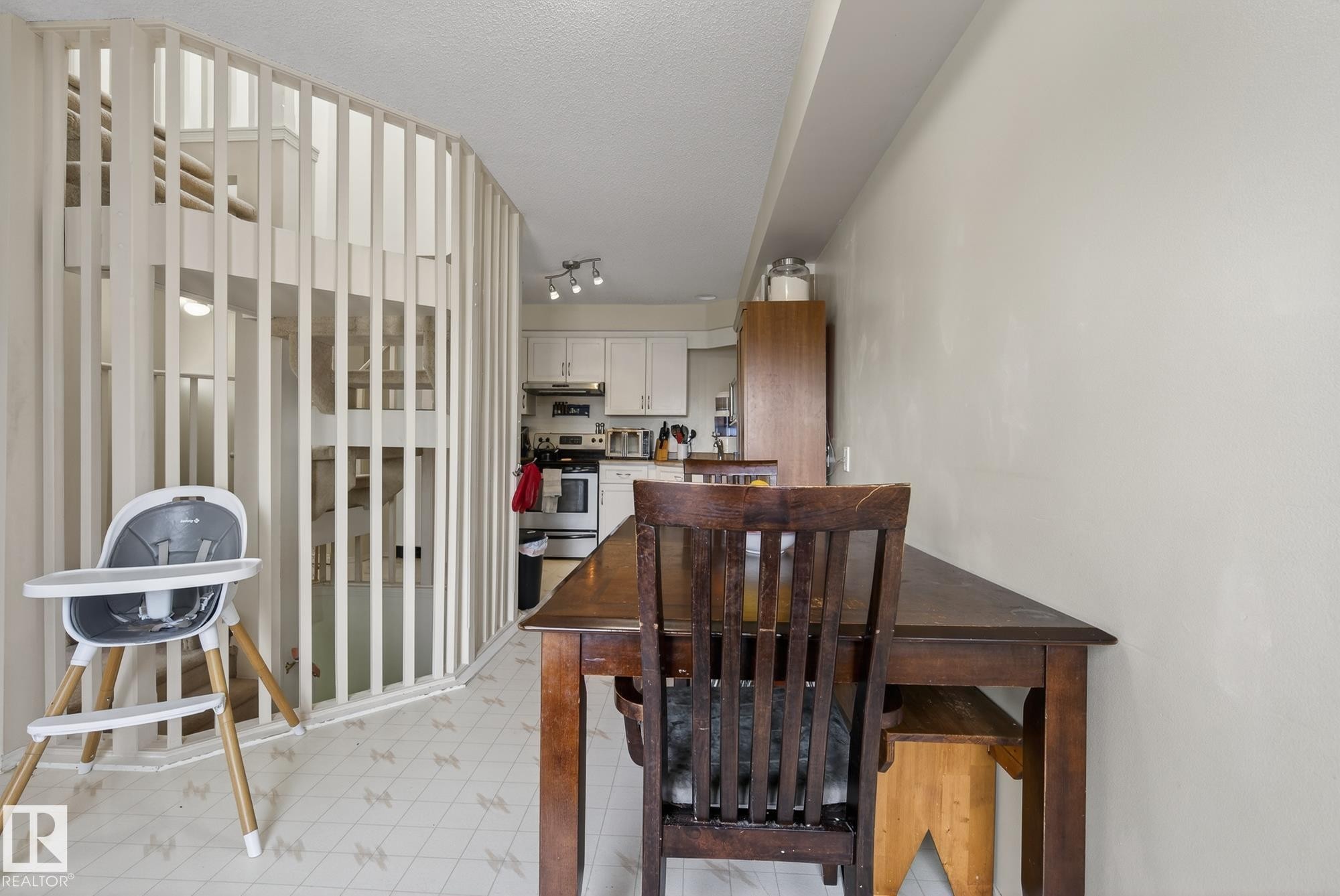 The property features an eat-in kitchen with white cabinetry and a white oven, alongside a dining area with a wooden table and chairs - 2006 Mill Woods Road E, Edmonton, AB - Indoor Photo Showing Dining Room
