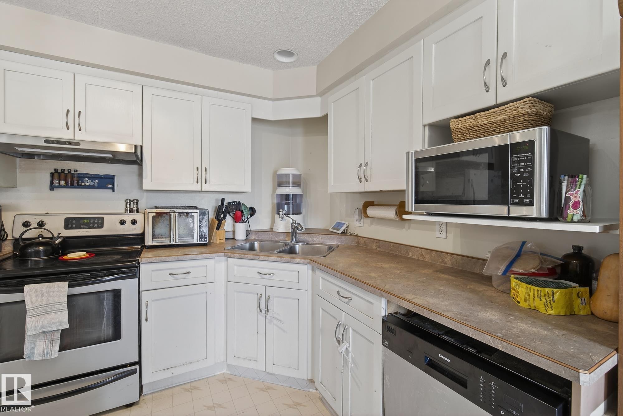 The kitchen features white cabinetry, a double basin stainless steel sink, and a stainless steel oven with an overhead range hood - 2006 Mill Woods Road E, Edmonton, AB - Indoor Photo Showing Kitchen With Double Sink