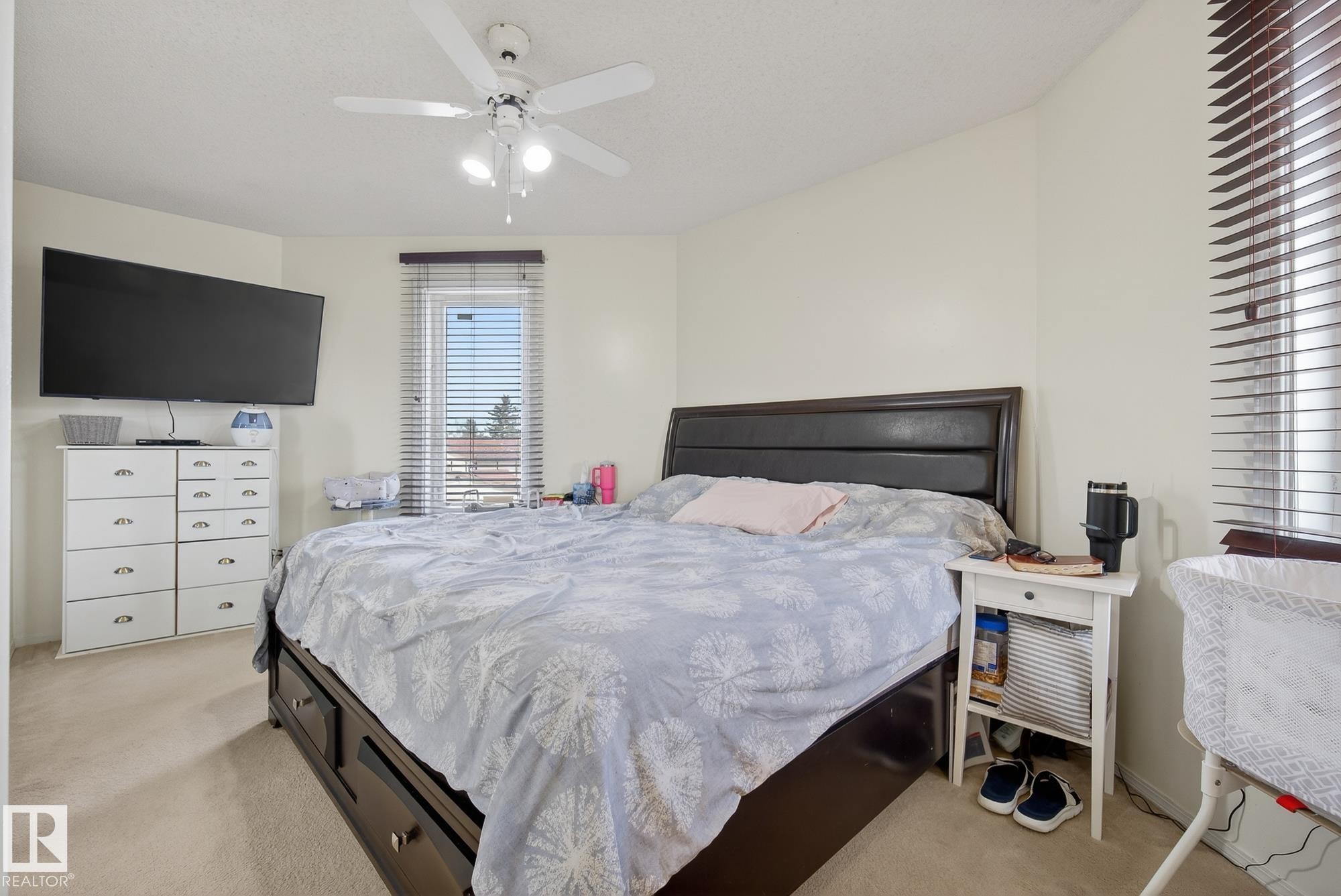 A well-lit bedroom featuring light-colored walls and carpeting, with a ceiling fan providing air circulation - 2006 Mill Woods Road E, Edmonton, AB - Indoor Photo Showing Bedroom