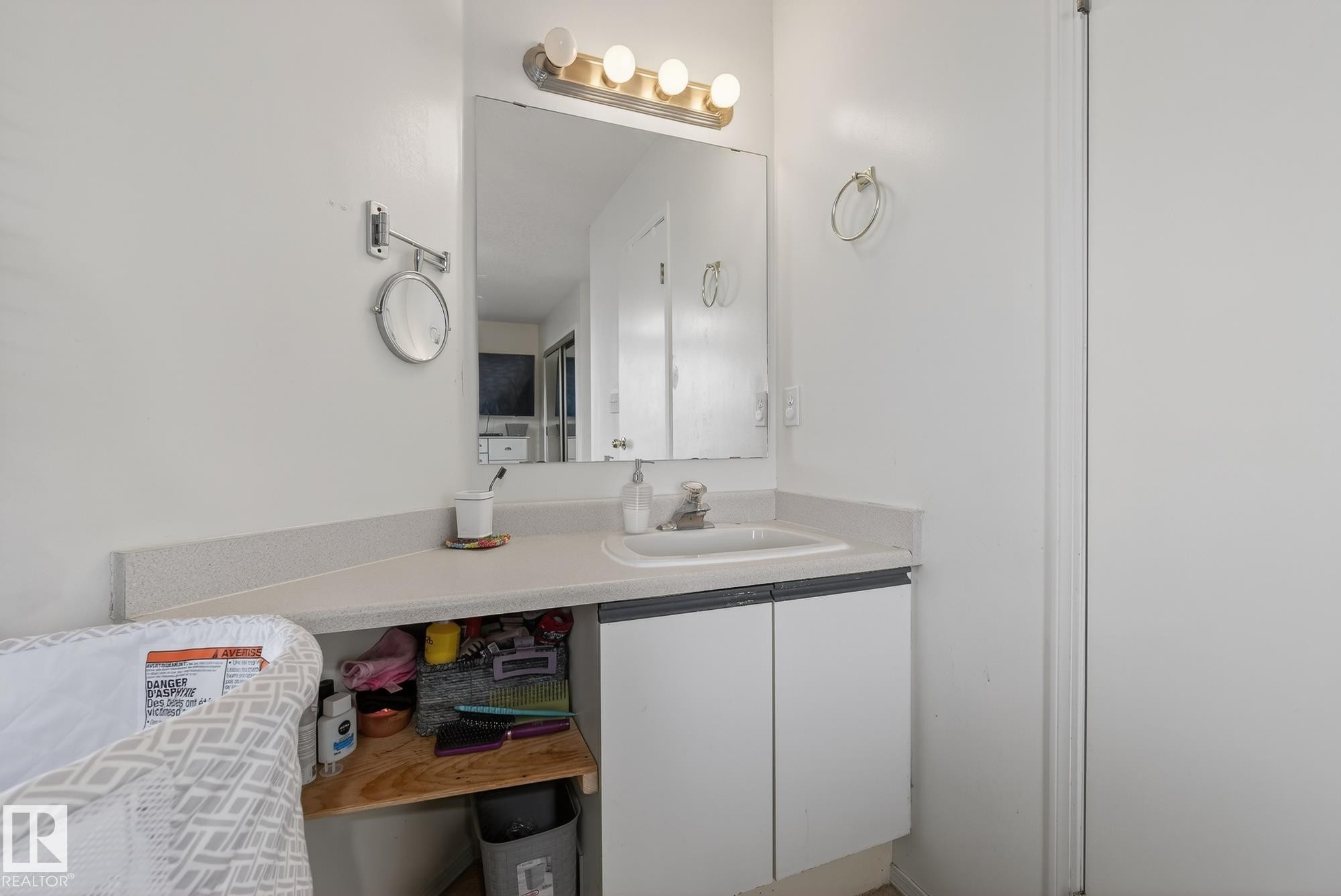The bathroom features a vanity with a white countertop and a built-in sink, illuminated by a light fixture above a mirror - 2006 Mill Woods Road E, Edmonton, AB - Indoor Photo Showing Bathroom