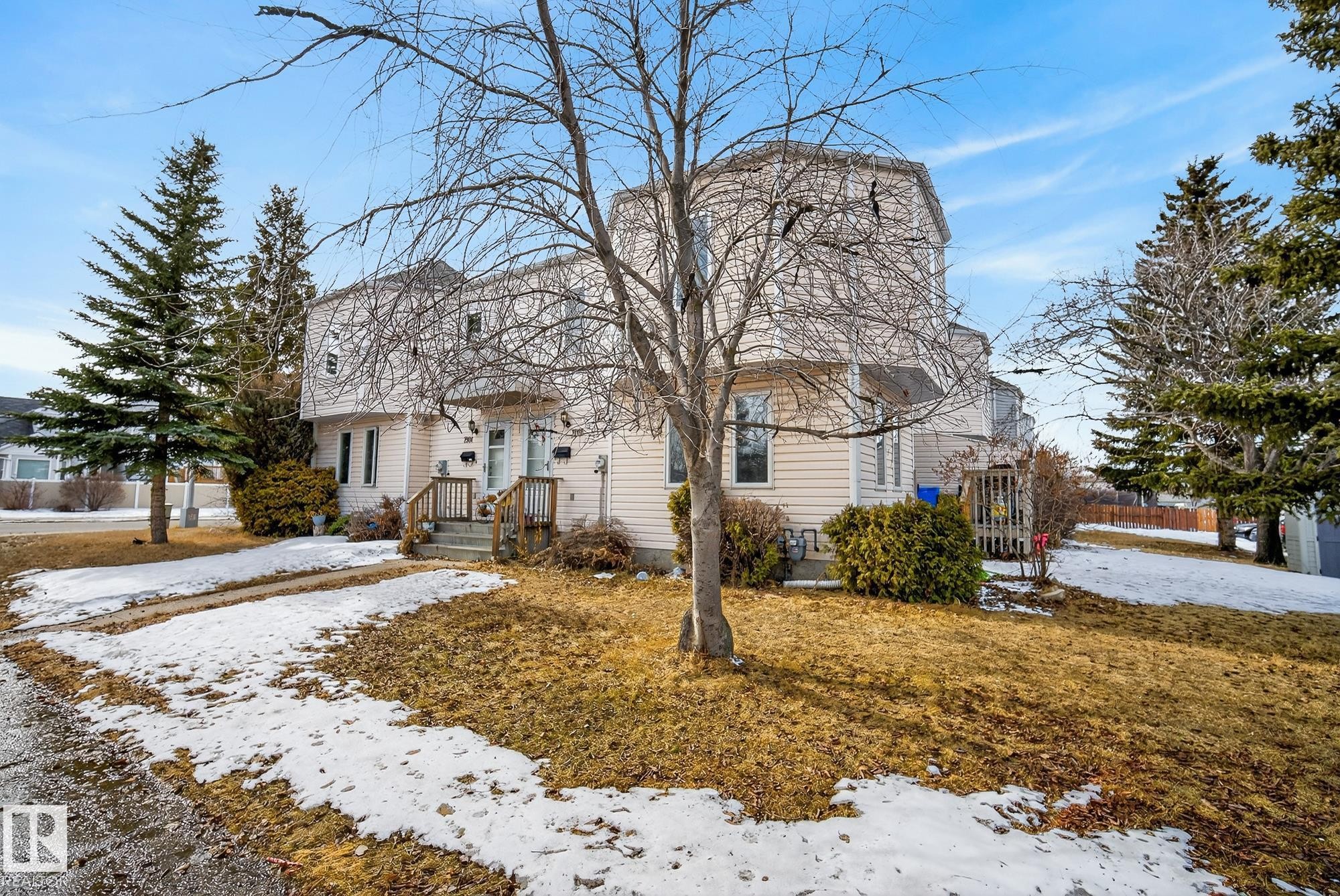 The property features a light-colored exterior, an entry with wooden steps and railing, and mature trees on the surrounding grounds - 2006 Mill Woods Road E, Edmonton, AB - Outdoor
