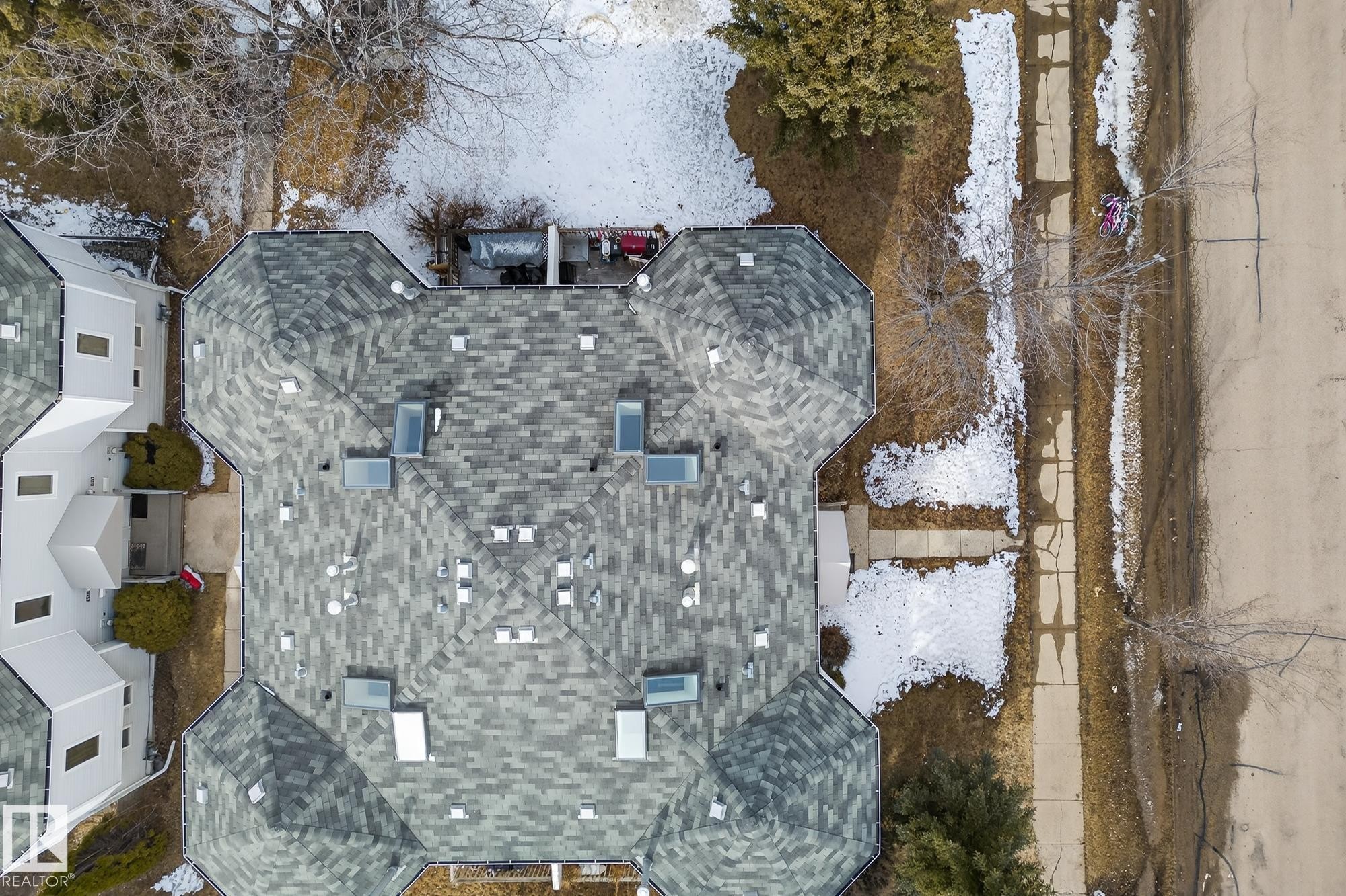 Aerial view of the property showcasing a grey shingled roof with several skylights, and a paved street and sidewalk running alongside - 2006 Mill Woods Road E, Edmonton, AB - Outdoor