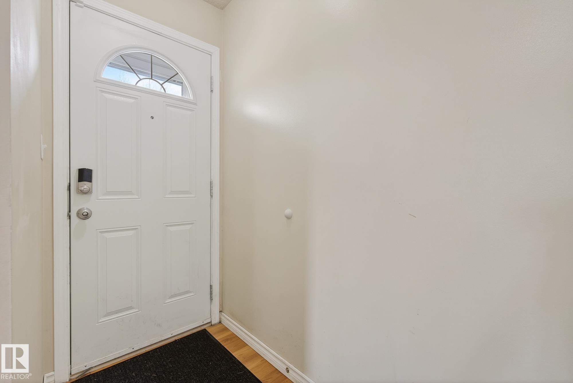 The property features a white panel door with an arched window, a smart lock, and light-colored walls - 2006 Mill Woods Road E, Edmonton, AB - Indoor Photo Showing Other Room