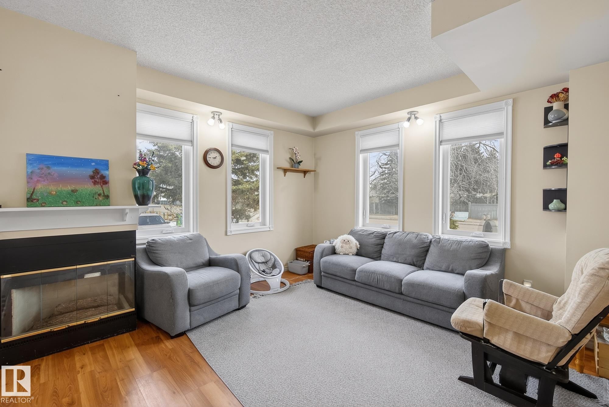 Living area featuring light-colored walls, a prominent fireplace with a dark surround, and a series of windows providing natural light - 2006 Mill Woods Road E, Edmonton, AB - Indoor Photo Showing Living Room With Fireplace