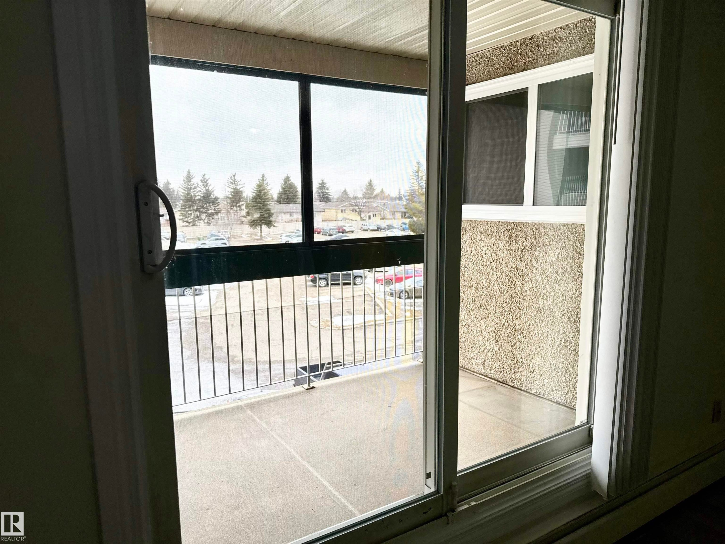 Sliding glass doors open to a private balcony with a metal railing, offering views of distant trees and a parking area - 307 1620 48 Street, Edmonton, AB