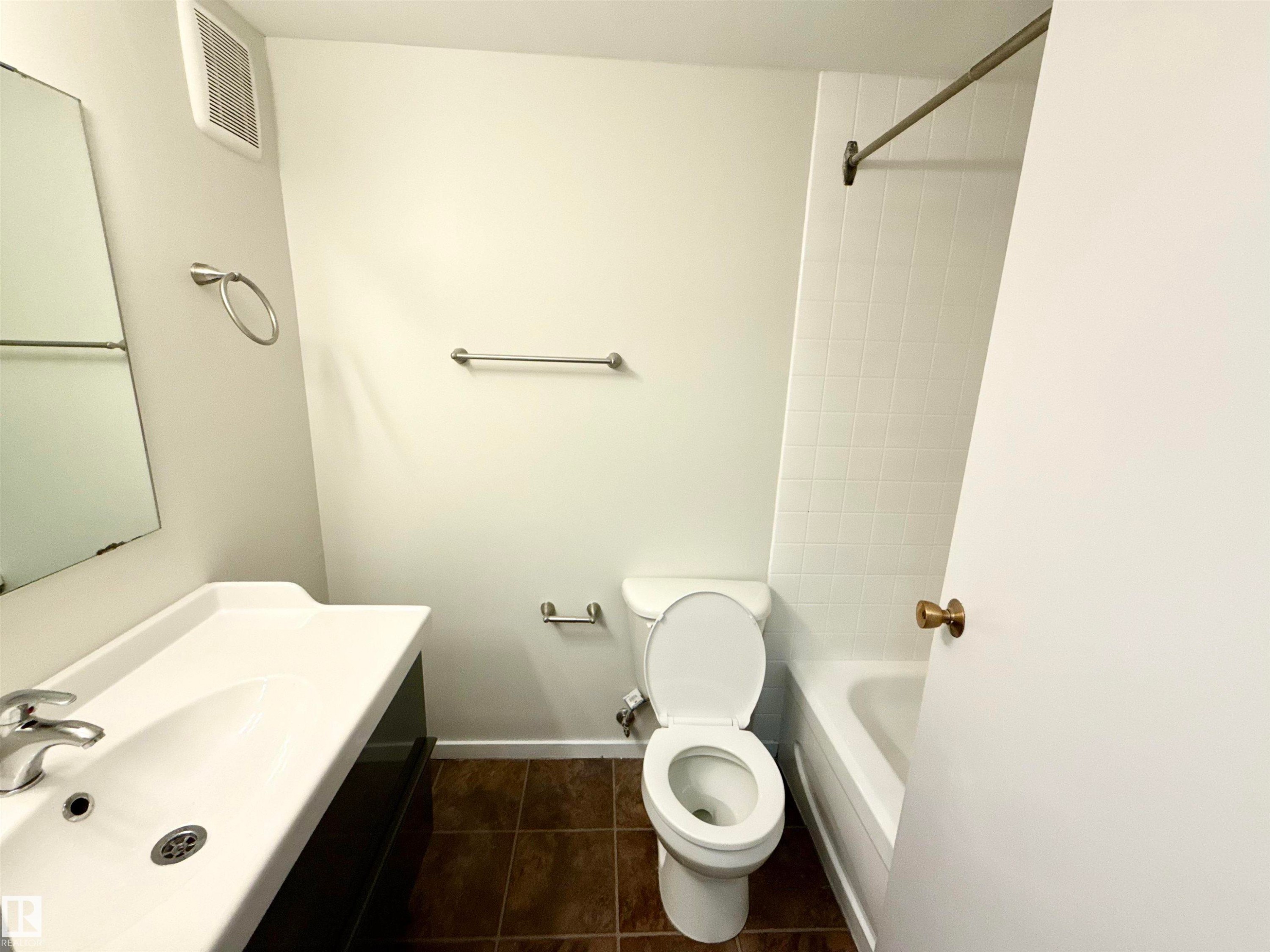 The bathroom features a vanity with an integrated sink, a toilet, a bathtub with white subway tile surround, and brown tiled flooring - 307 1620 48 Street, Edmonton, AB