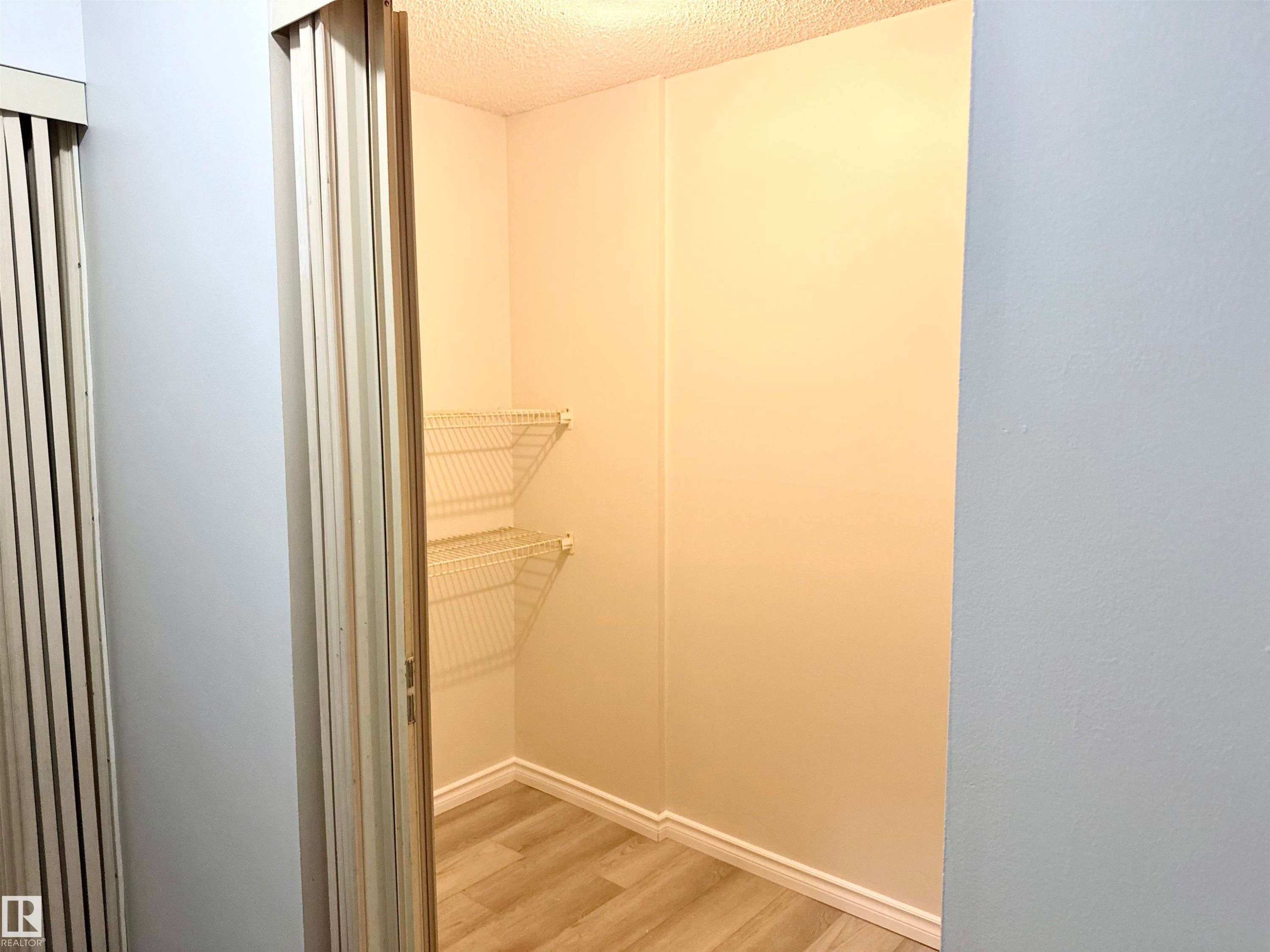 The property features a closet with bi-fold doors, wire shelving, and light wood-style flooring - 307 1620 48 Street, Edmonton, AB