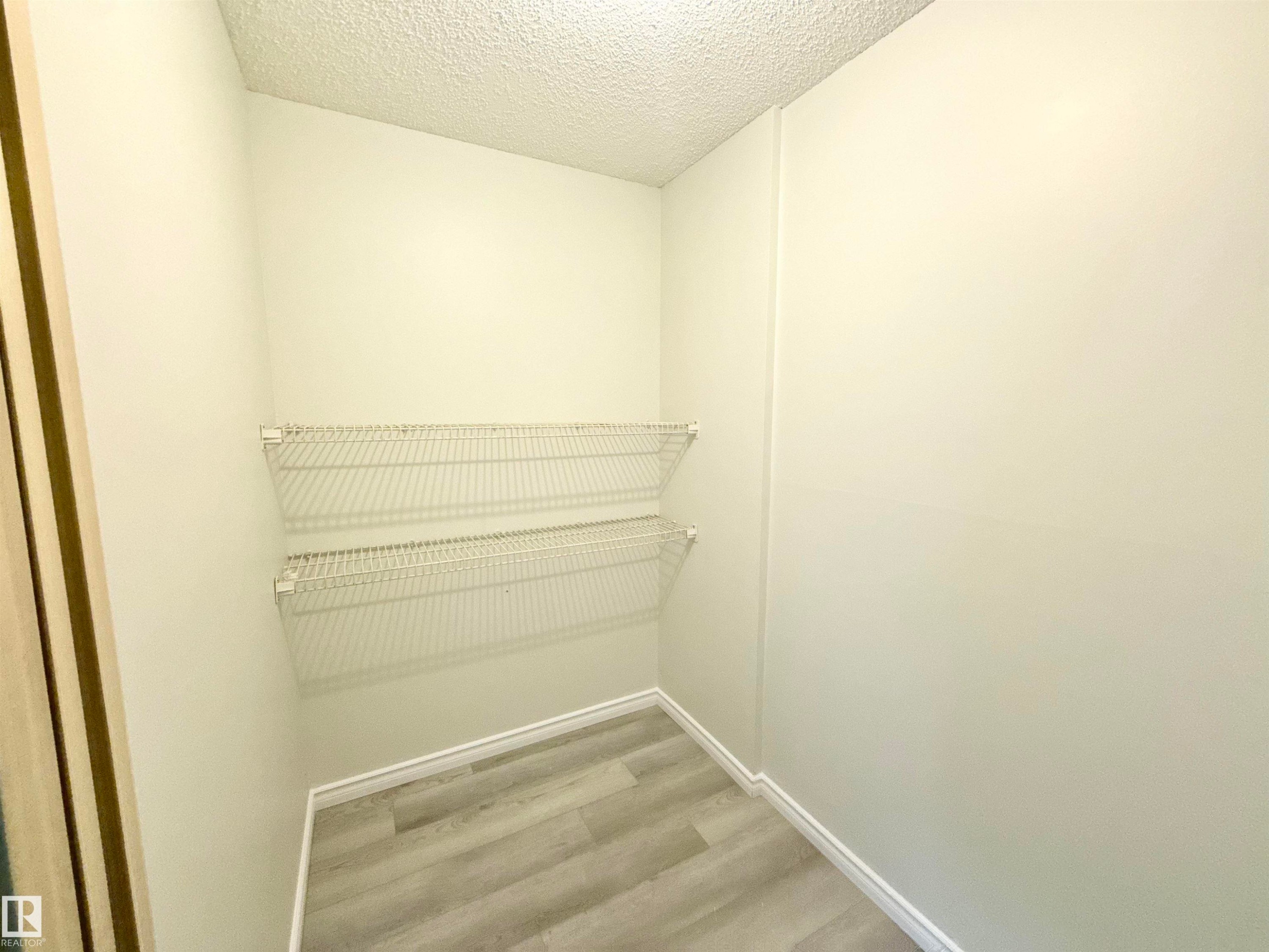 This space features light-colored walls, wire shelving, and wood-look flooring - 307 1620 48 Street, Edmonton, AB