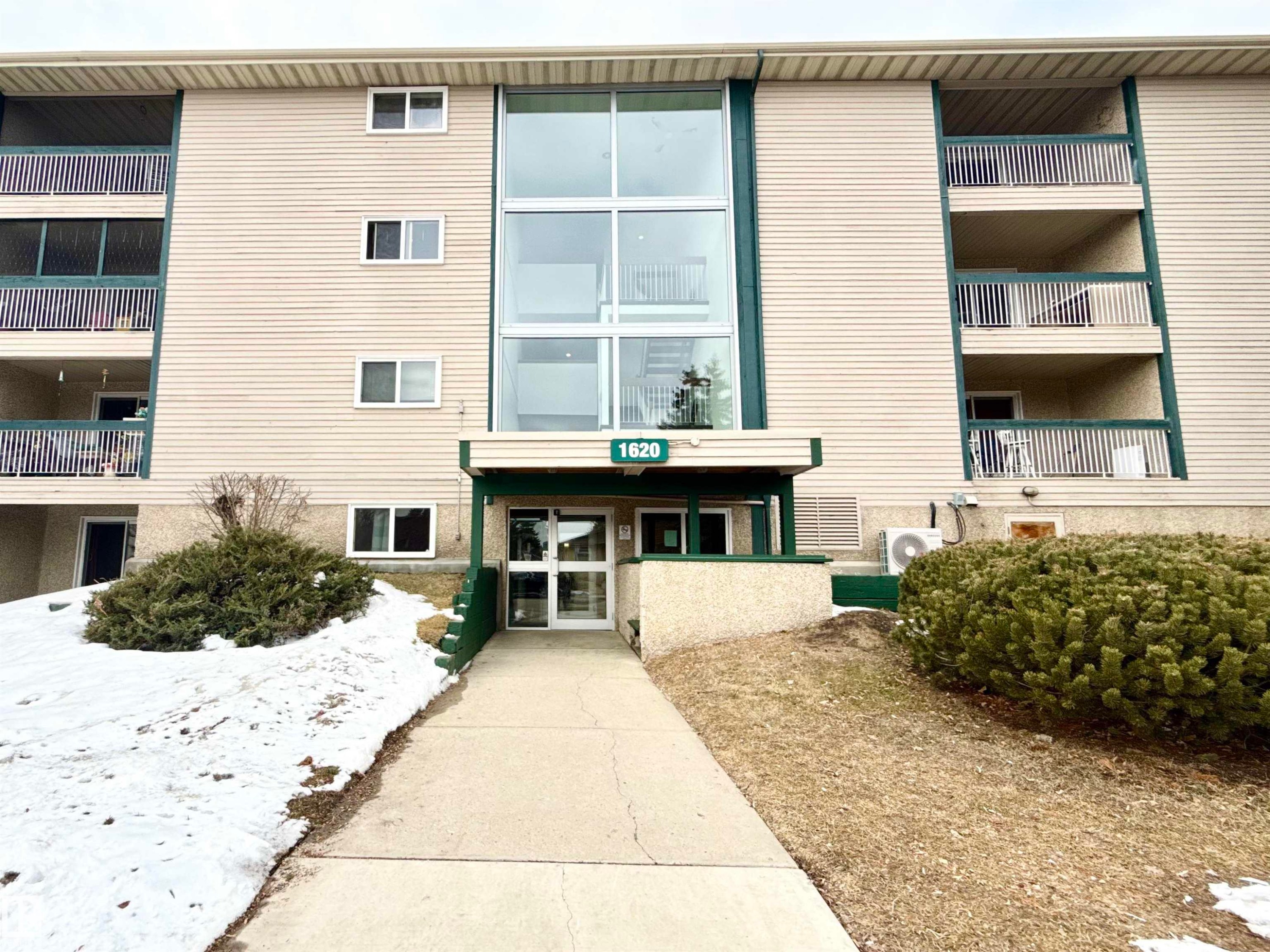 The property features a multi-story exterior with horizontal siding, a prominent glass entrance, and individual balconies with railings - 307 1620 48 Street, Edmonton, AB