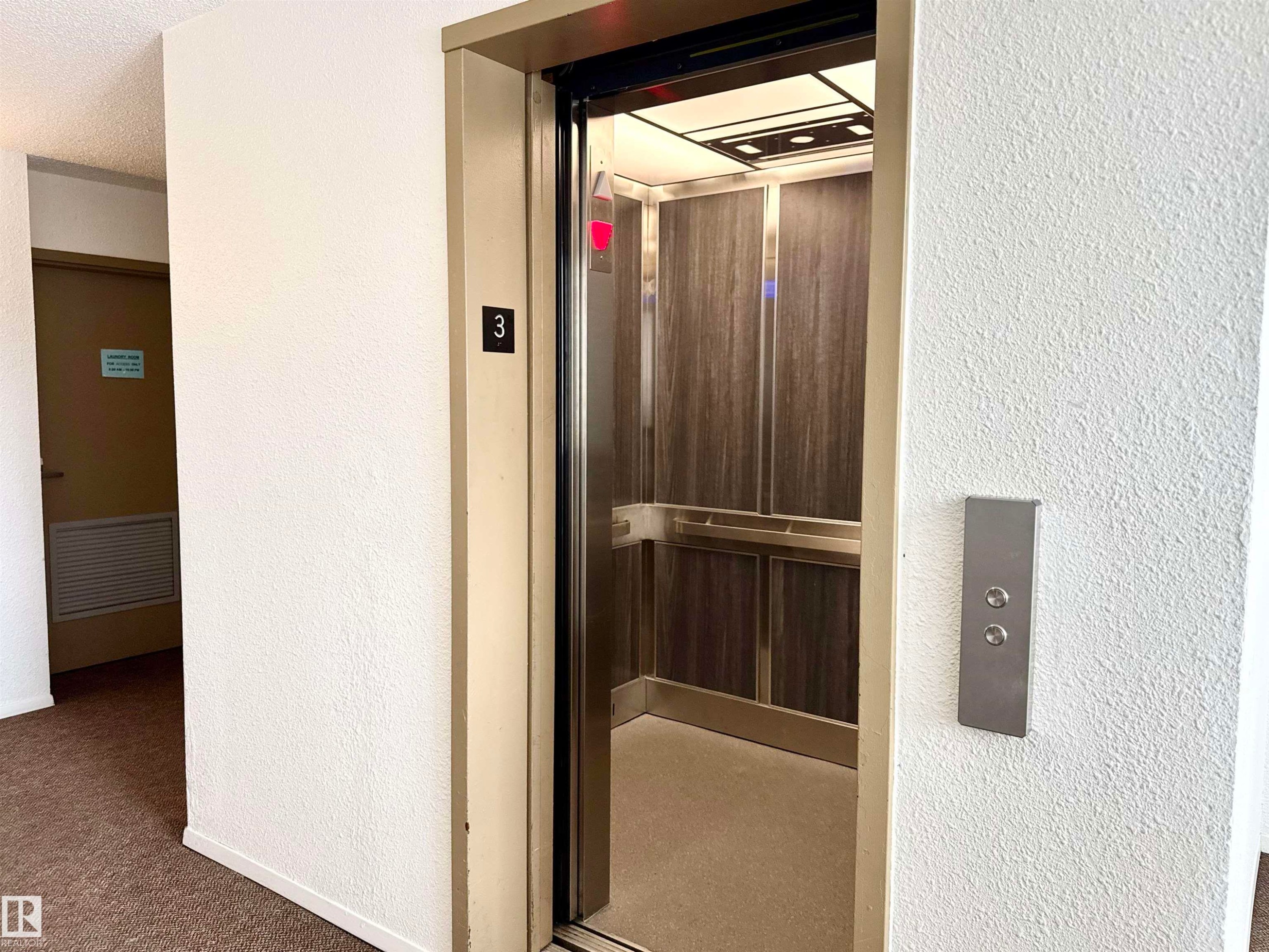 The property provides elevator access, featuring a modern elevator car with wood-paneled walls and a mirrored ceiling - 307 1620 48 Street, Edmonton, AB