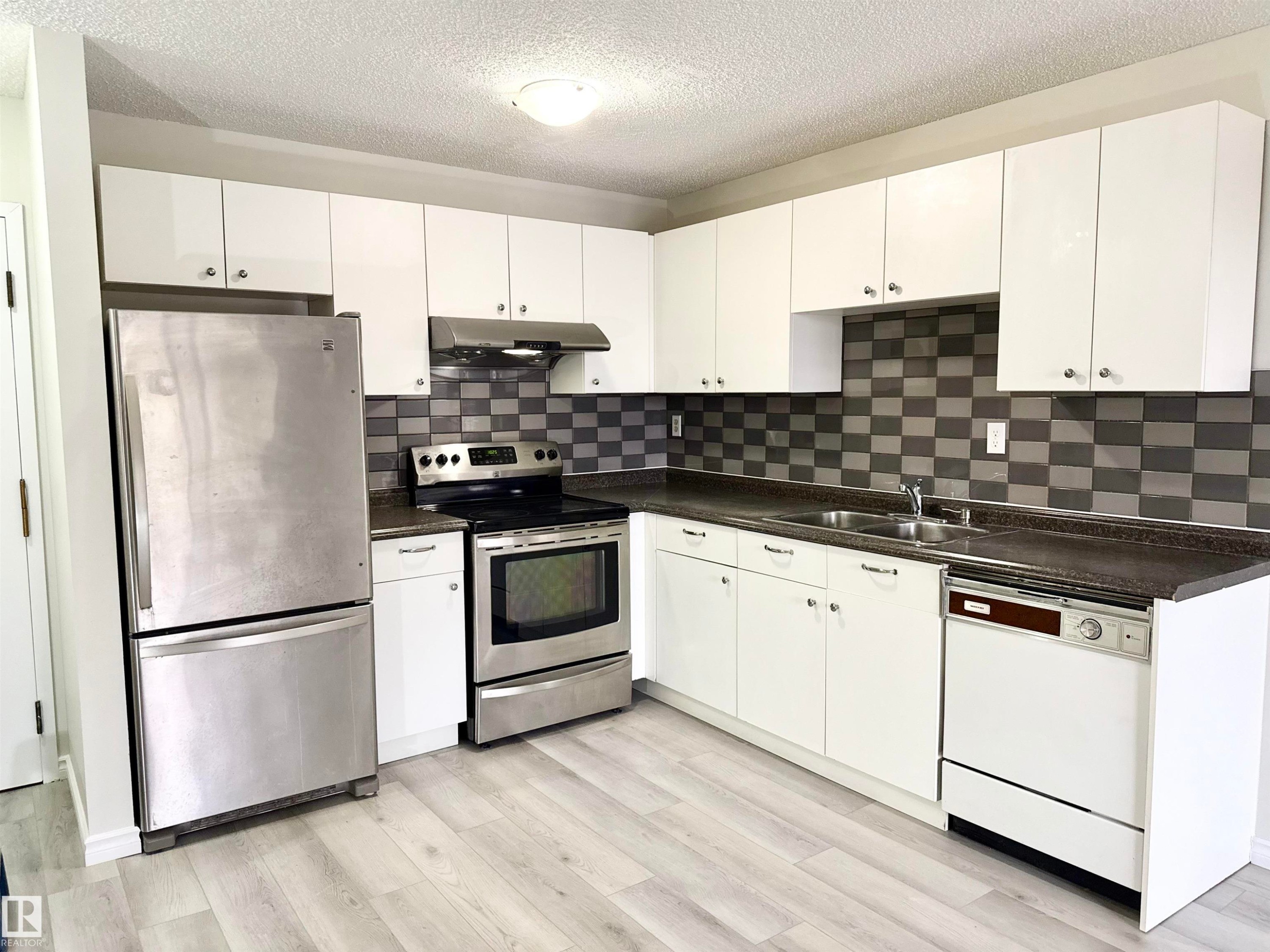 The kitchen features white cabinetry, a stainless steel refrigerator, and a stainless steel oven with a range hood - 307 1620 48 Street, Edmonton, AB