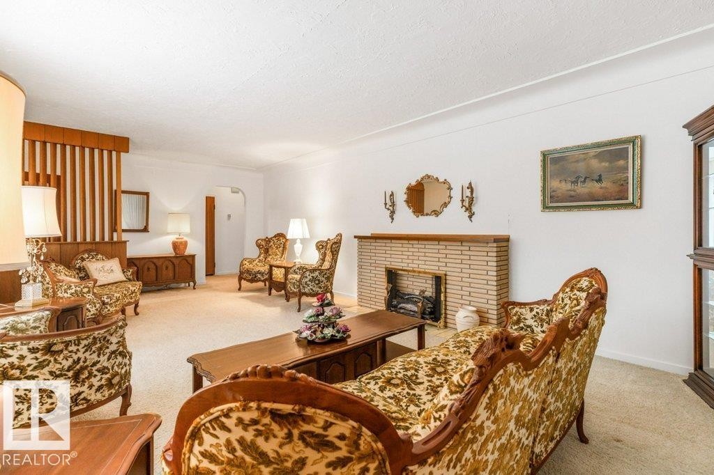 Living area with light colored carpet, arched walkways, a brick fireplace, and a textured ceiling - 8810 93 Street, Edmonton, AB - Indoor Photo Showing Living Room With Fireplace