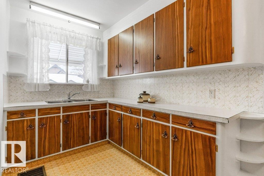 Kitchen featuring light countertops, open shelves, light flooring, tasteful backsplash, and brown cabinets - 8810 93 Street, Edmonton, AB - Indoor Photo Showing Kitchen With Double Sink