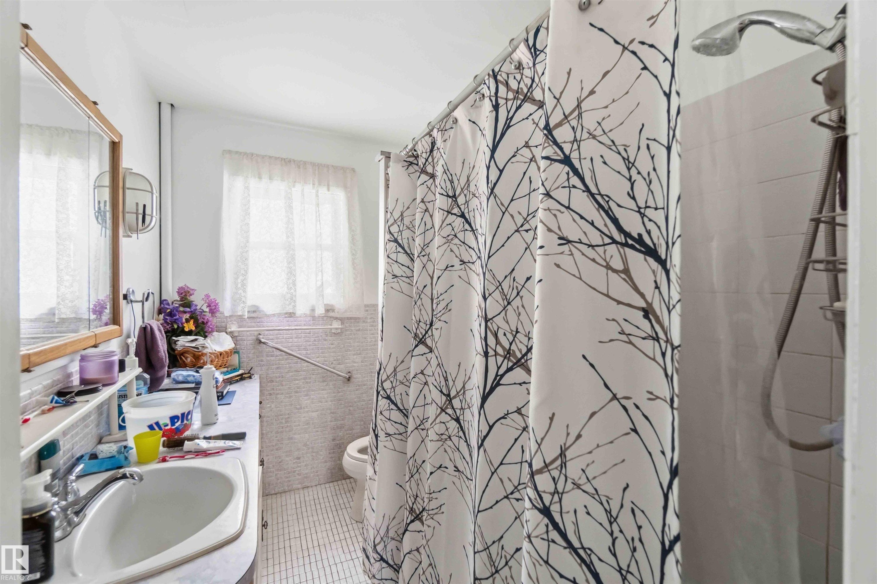 Bathroom featuring a vanity with a sink, a window with curtains, and a shower with a showerhead - 10186 143 Street, Edmonton, AB - Indoor Photo Showing Bathroom