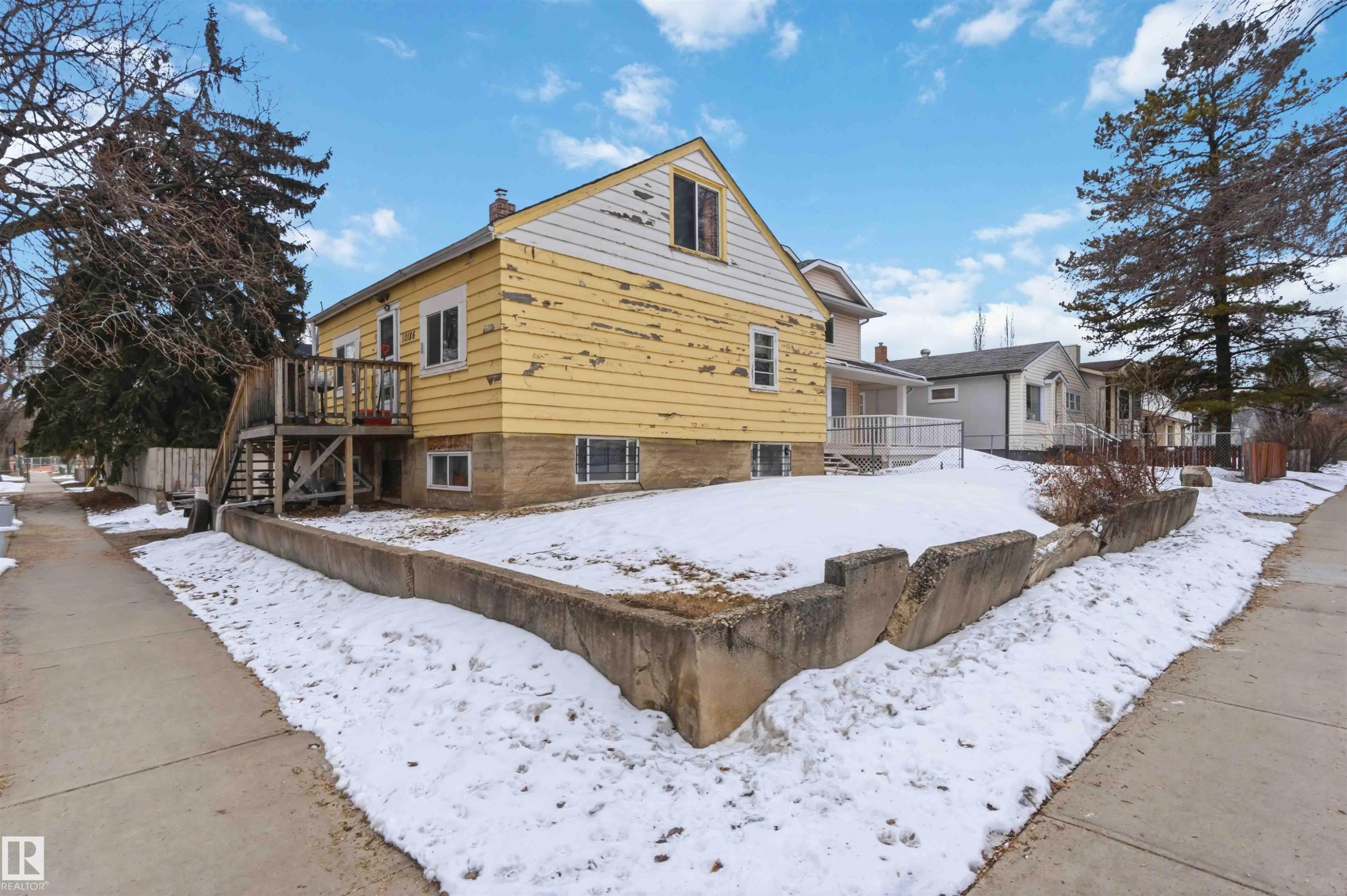 The property features a yellow exterior with white trim, multiple windows, and a raised wooden deck with stairs - 10186 143 Street, Edmonton, AB - Outdoor