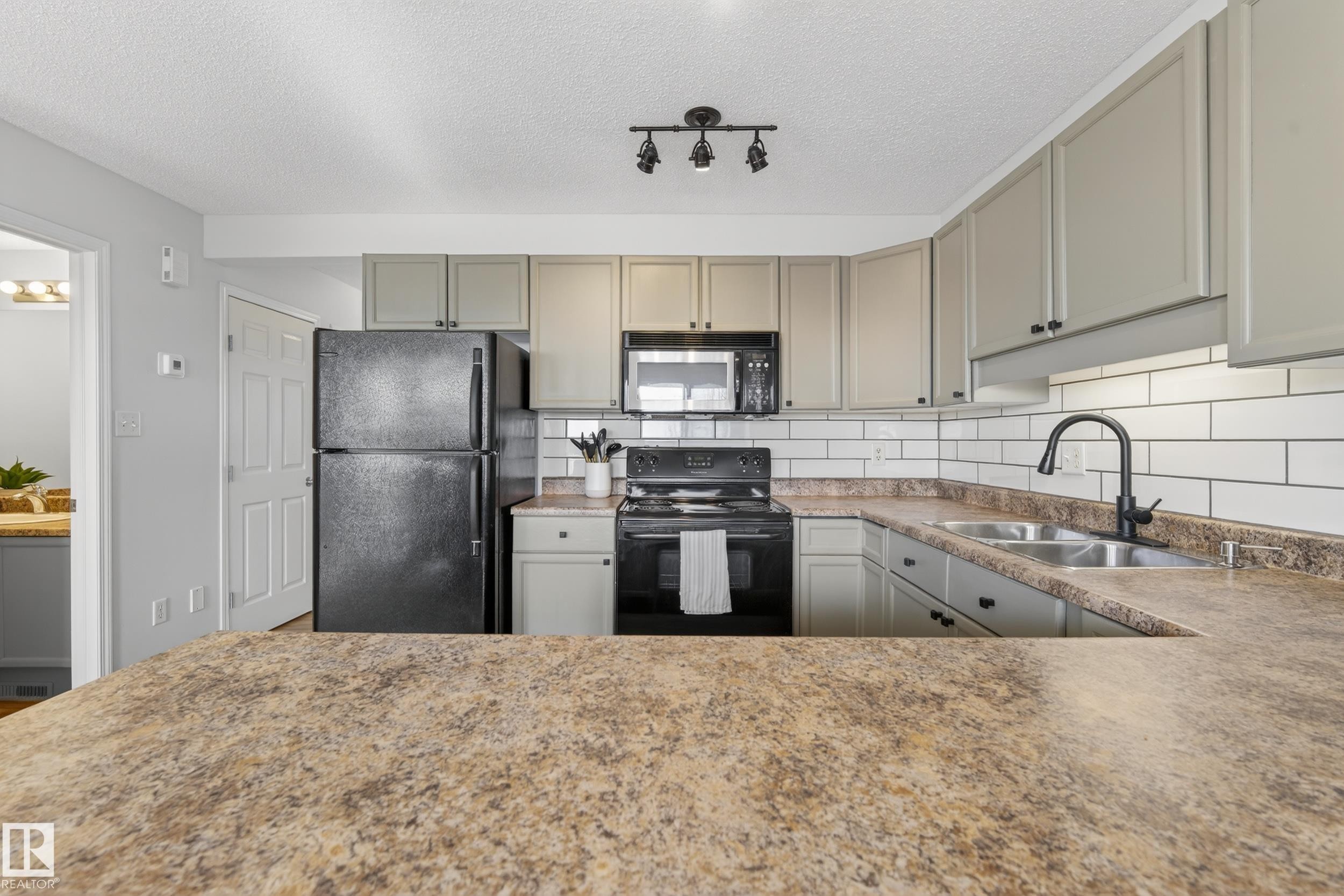 Kitchen featuring a dark countertop, subway tile backsplash, and light-colored cabinetry - 9051 Scott Crescent, Edmonton, AB