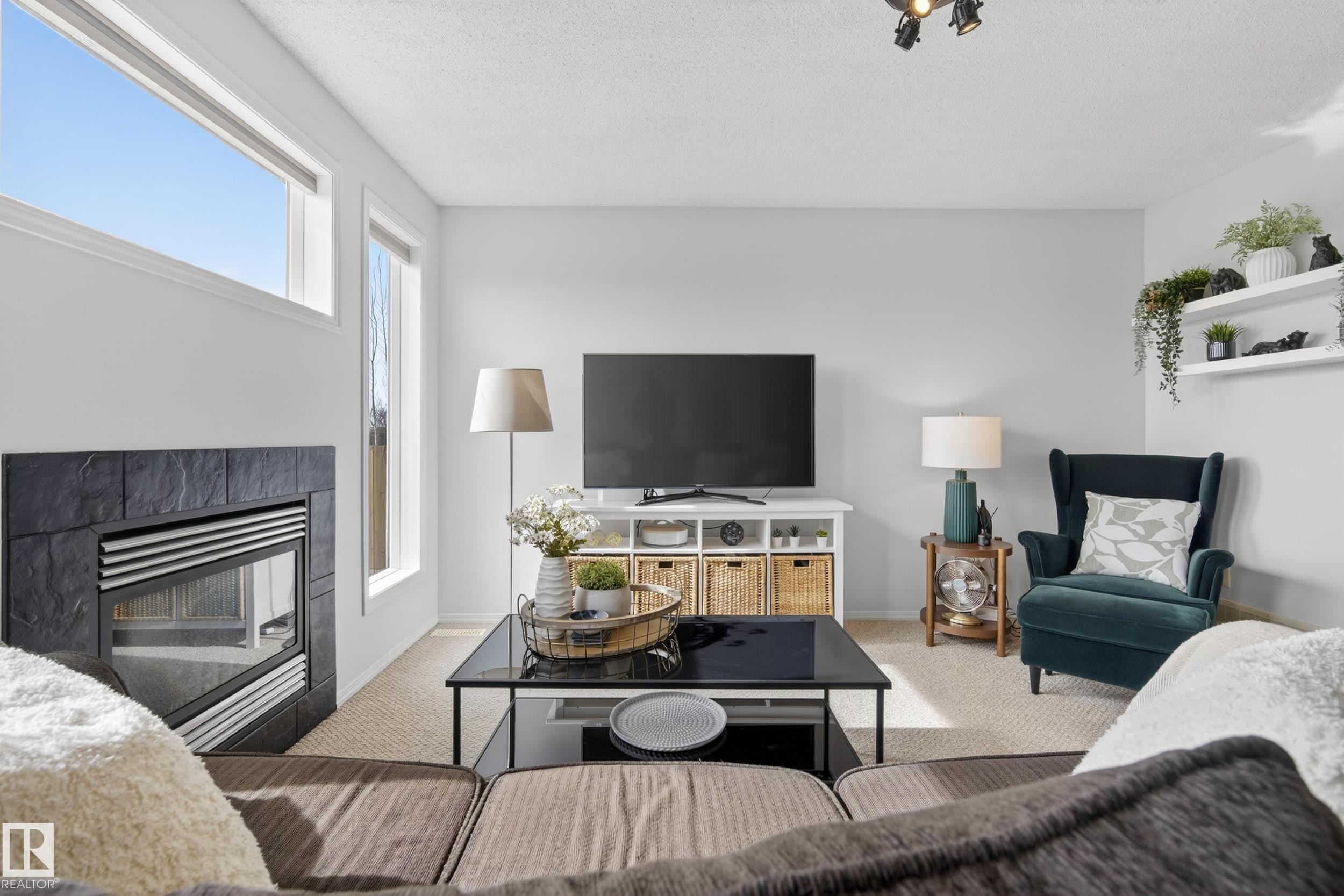 The living area features a built-in fireplace with a dark stone surround, tall windows providing natural light, and track lighting on the ceiling - 9051 Scott Crescent, Edmonton, AB