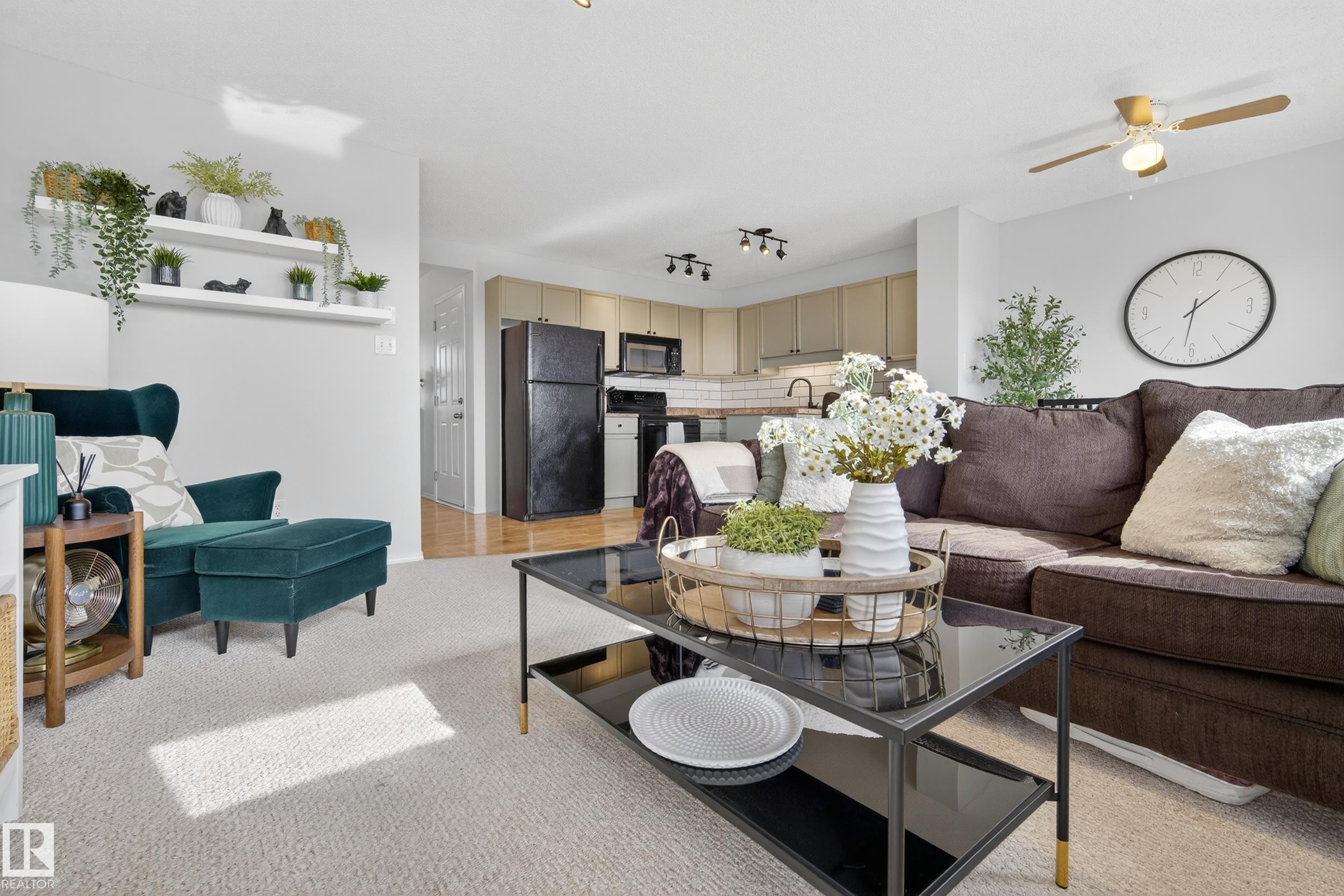 Open concept living area featuring a ceiling fan, carpeted flooring, and a view of the kitchen with light-colored cabinetry and black appliances - 9051 Scott Crescent, Edmonton, AB